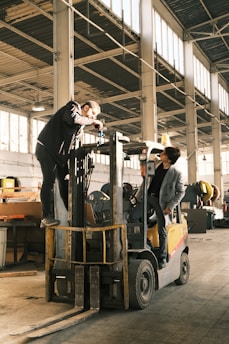A man standing on top of a forklift in a warehouse