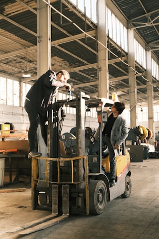 A man standing on top of a forklift in a warehouse