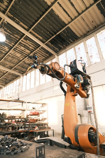 A large orange robot in a building with lots of tools