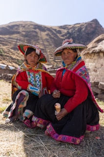 Two women sitting on the ground with mountains in the background