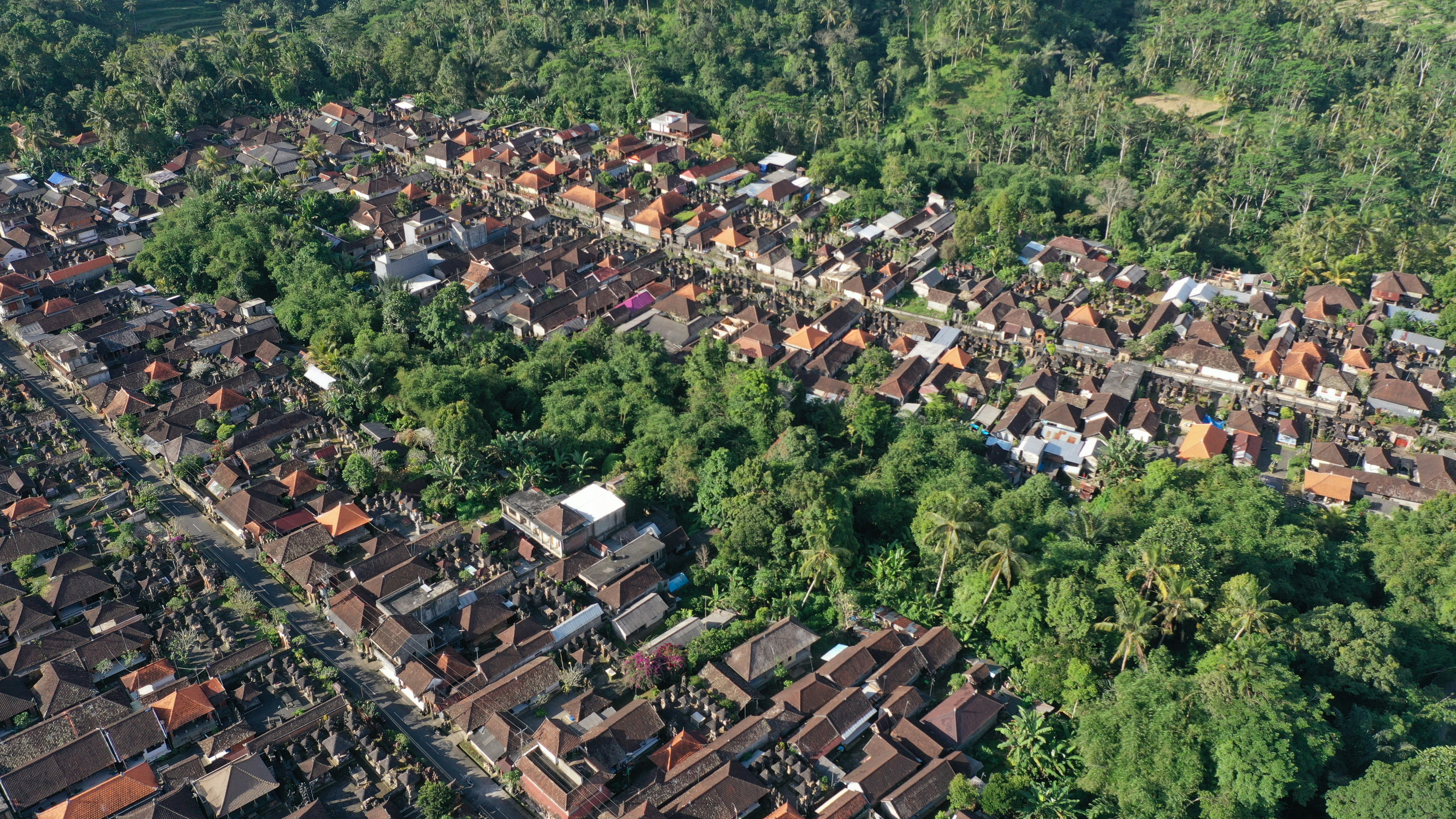 An aerial view of a newly constructed, well-planned residential township nestled amidst lush green hills, with clean roads and uniform houses.