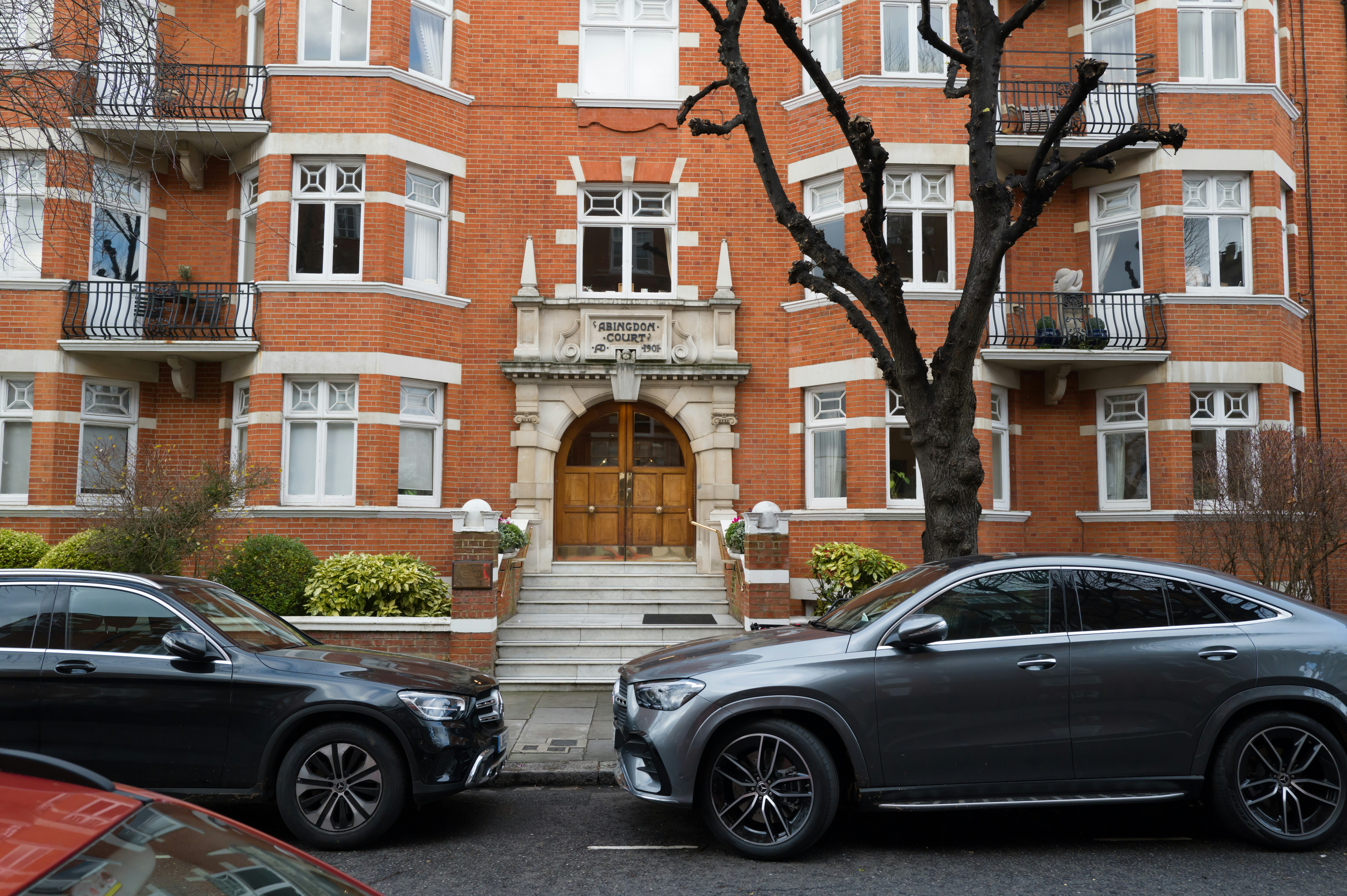 A realistic photo of official vehicles with 'Vigilance' written on them, parked outside a large residential building with uniformed officers entering.