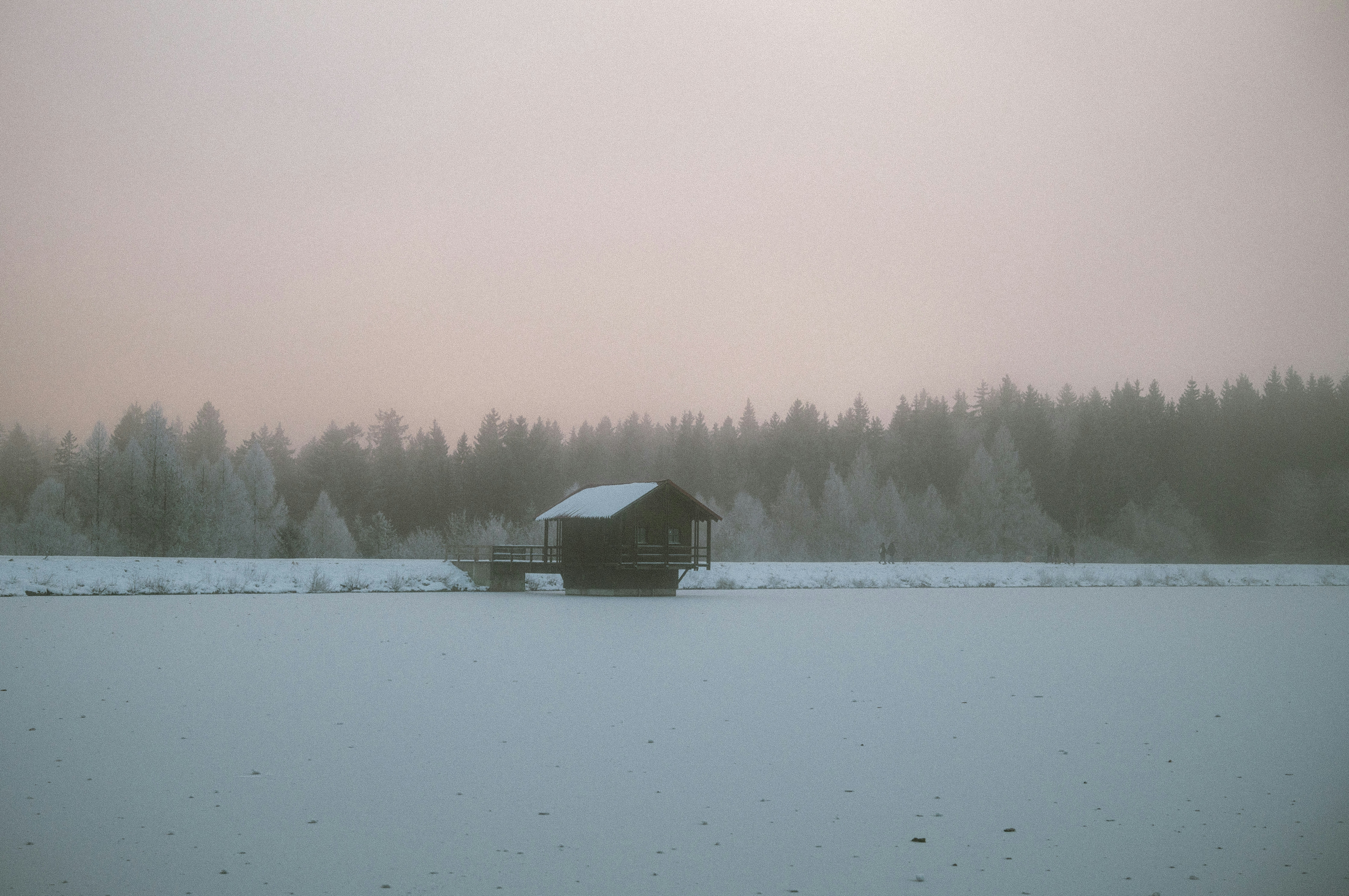 A barn in a snowy field with trees in the background