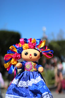 A small mexican doll with a blue dress and colorful hair