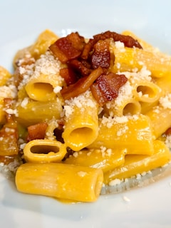 A white plate topped with pasta and bacon