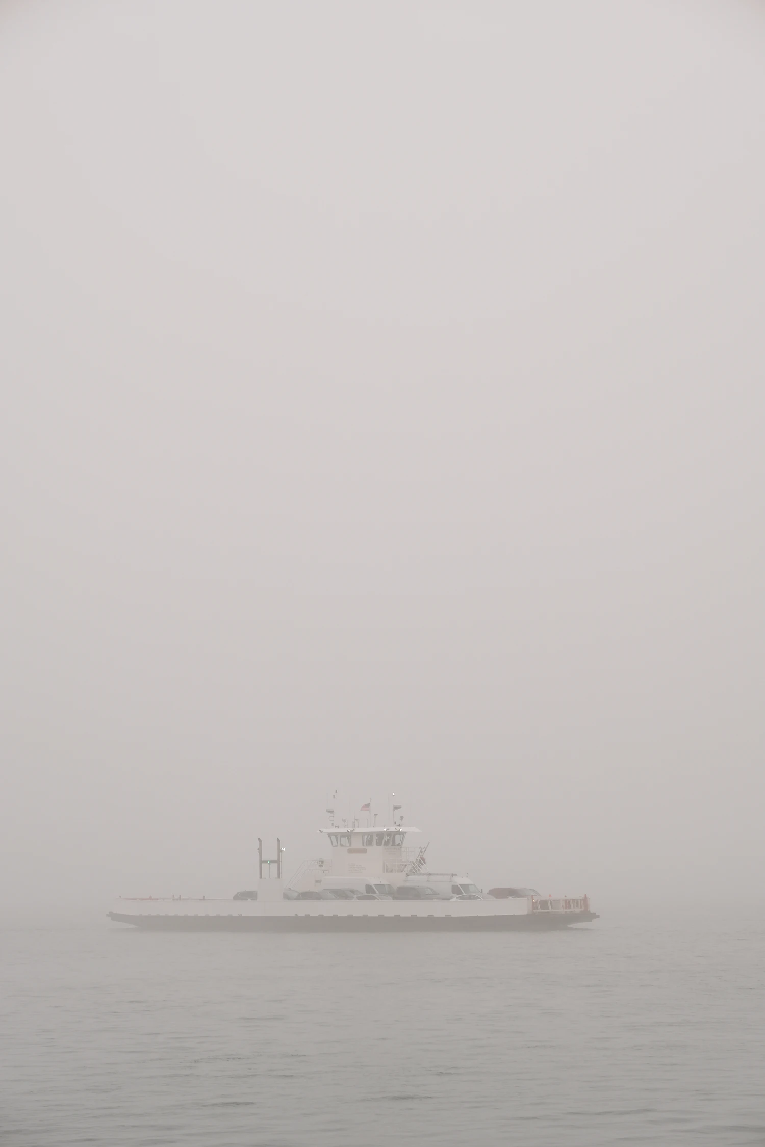 A white ferry crossing a lake in thick morning fog, barely separated from the sky