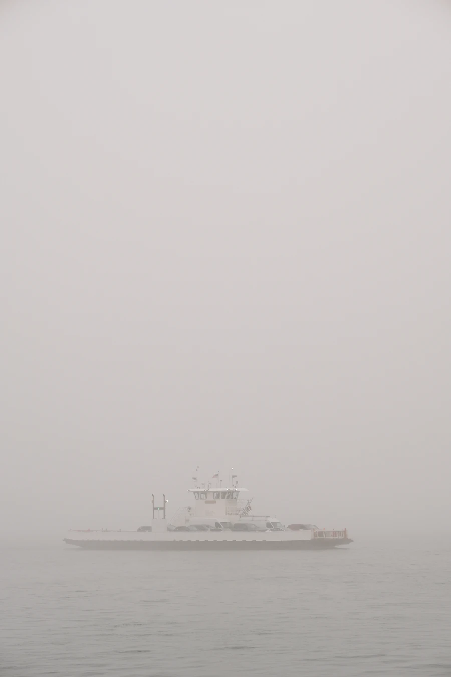 A white ferry crossing a lake in thick morning fog, barely separated from the sky