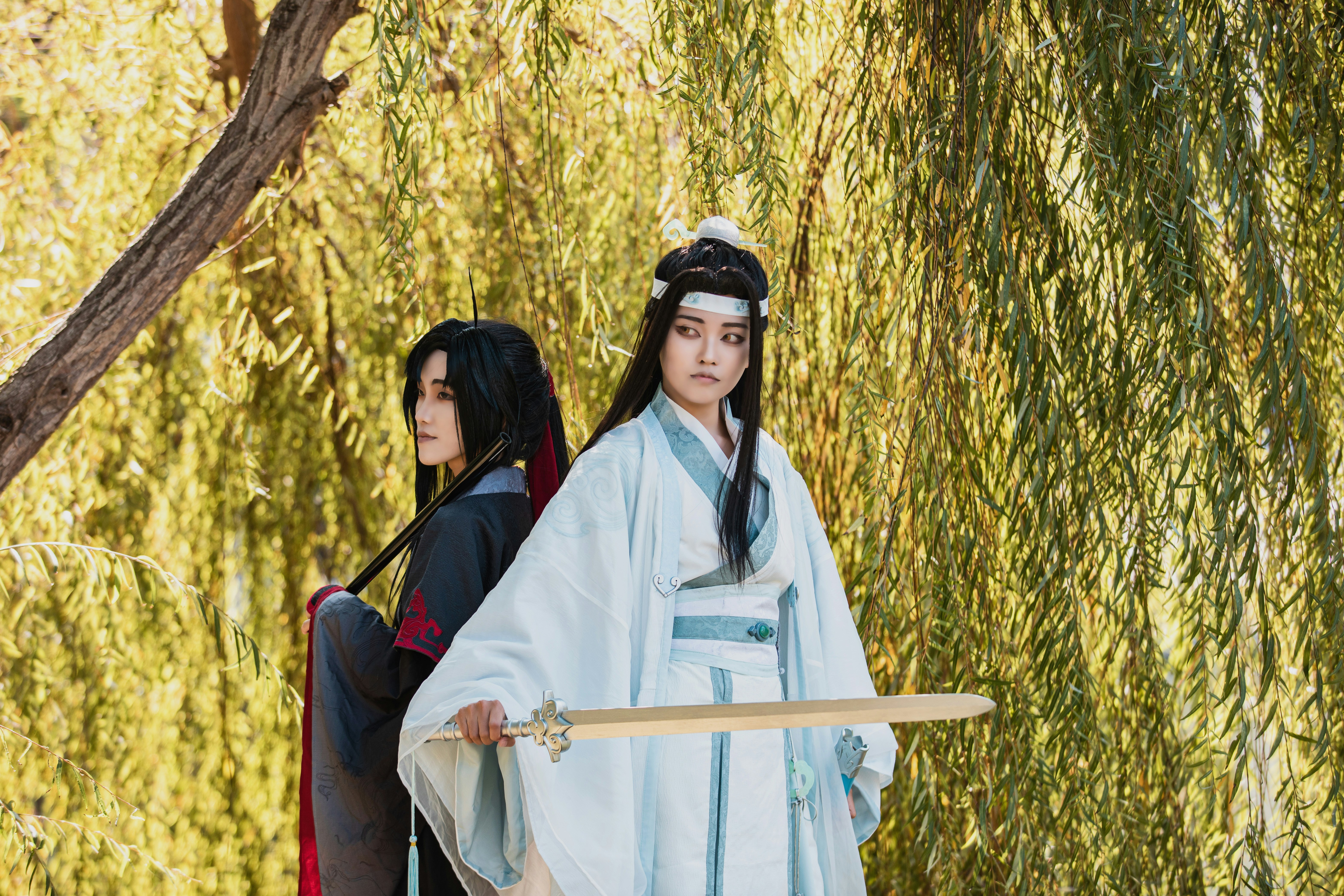 Two women dressed in traditional japanese costumes standing in front of a willow tree