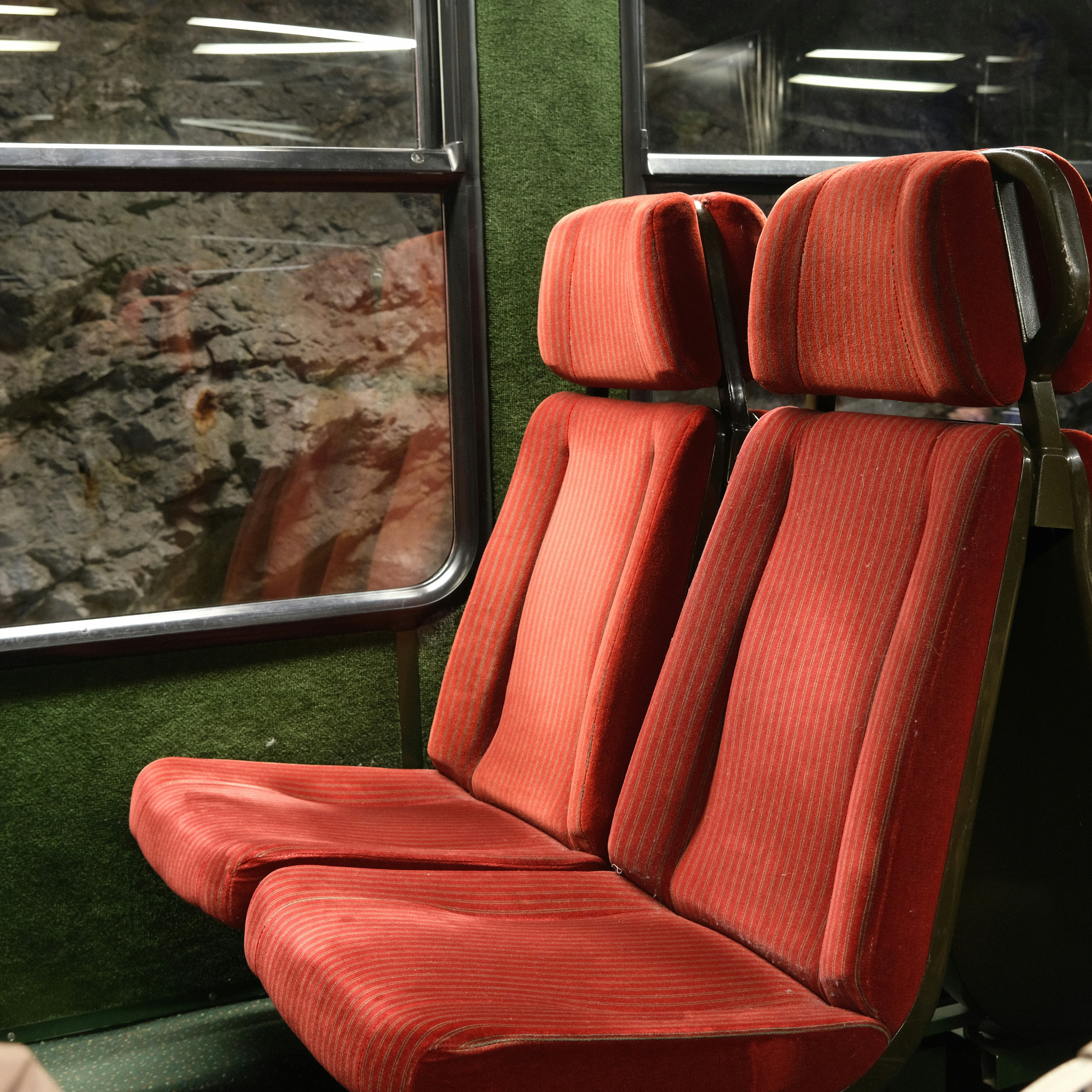 A red seat on a train next to a window