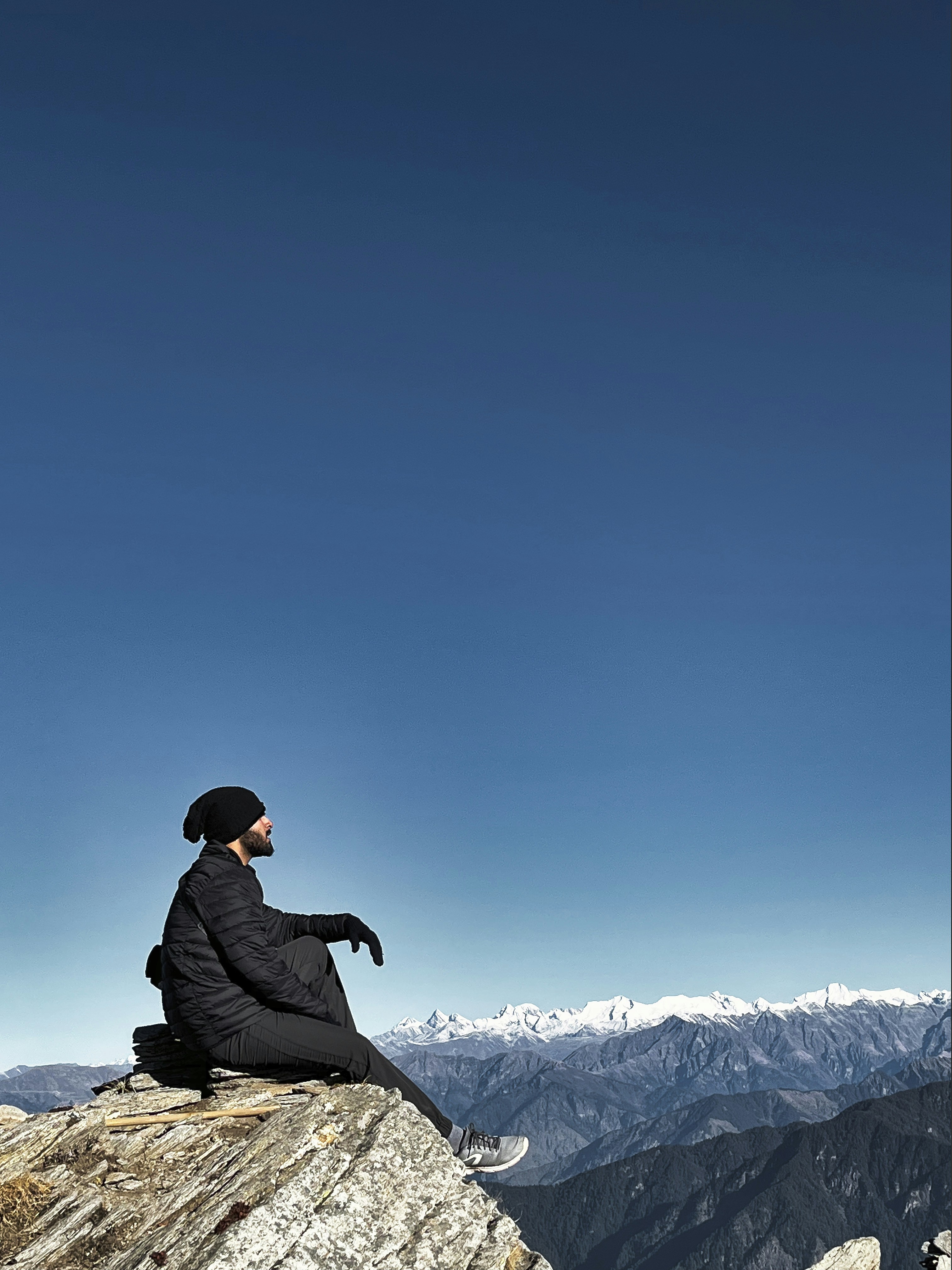 A person sitting on top of a rock on top of a mountain