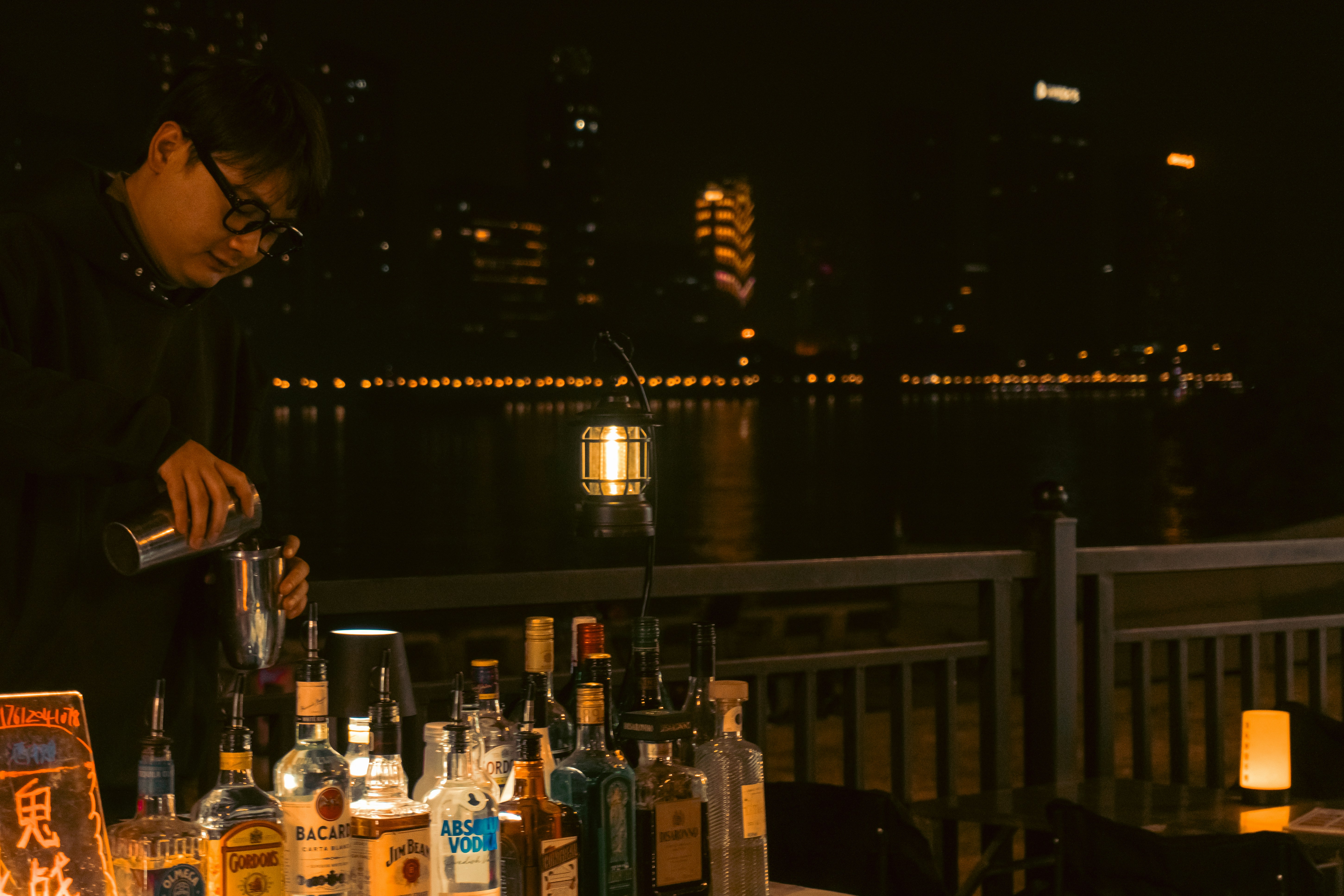 Bartender beside a table of bottles at night
