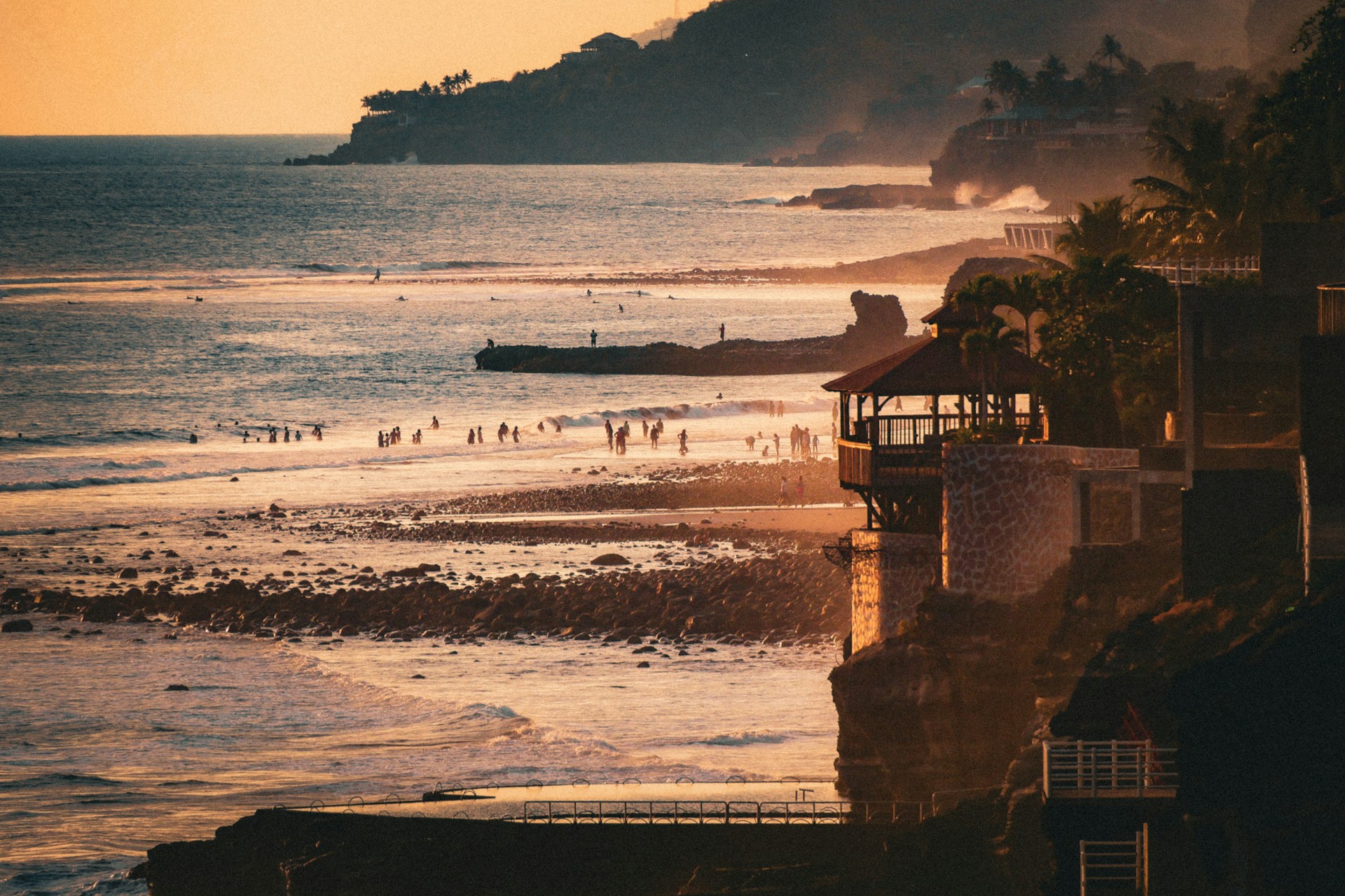 A sunset view of a beach with people in the water
