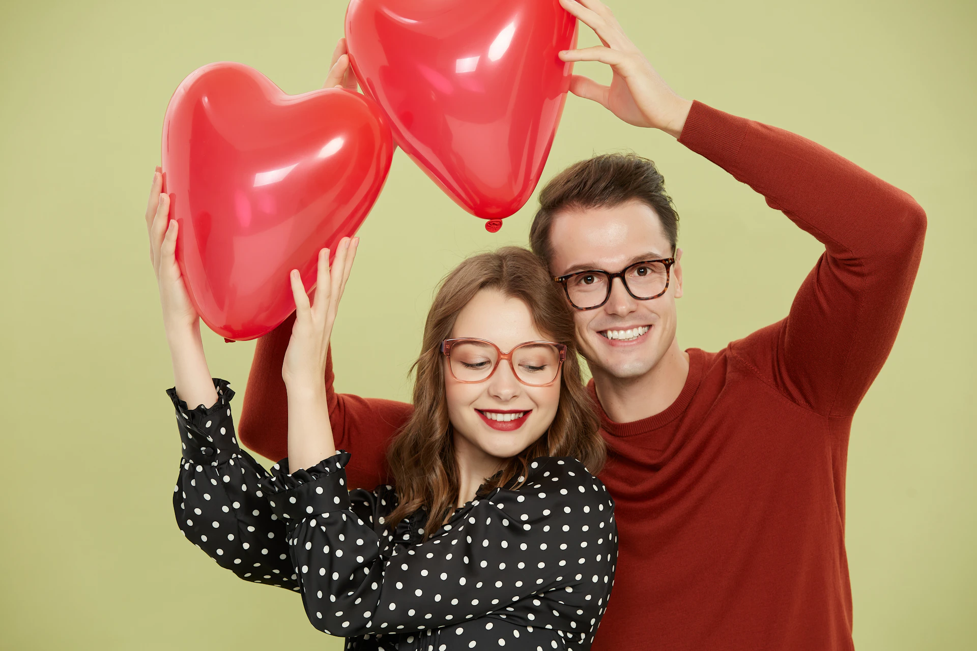 A man and a woman holding red heart shaped balloons