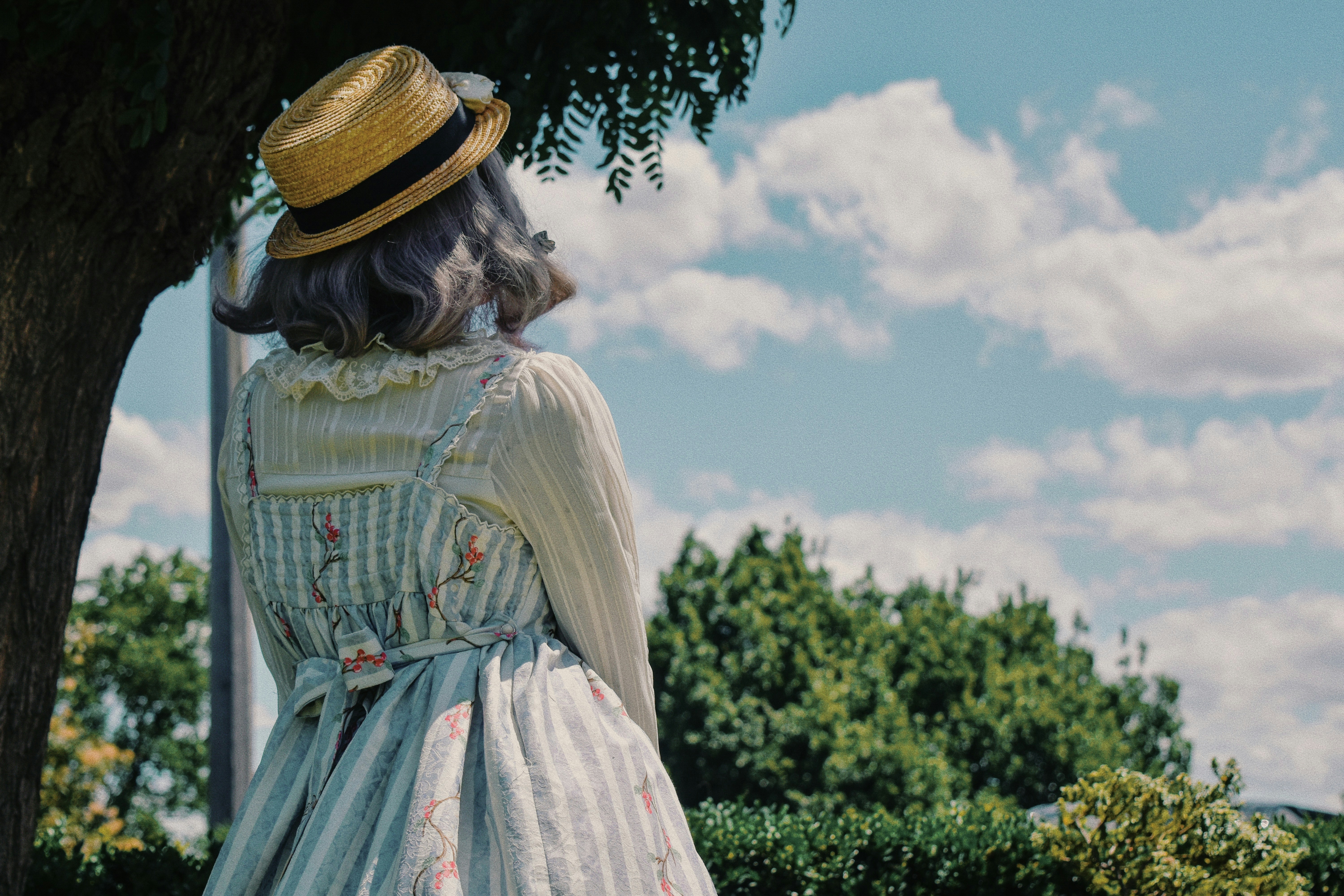 A woman in a dress and hat standing under a tree