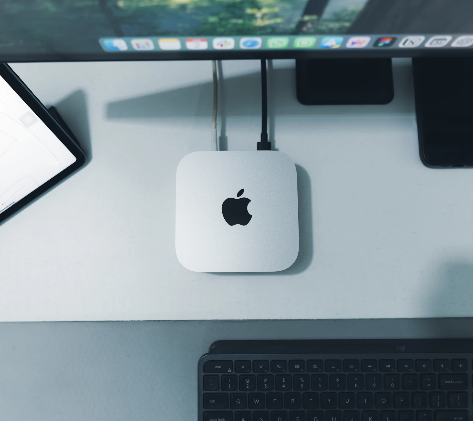 Silver Mac mini seen from above on a white desk mat with two cables plugged into its back