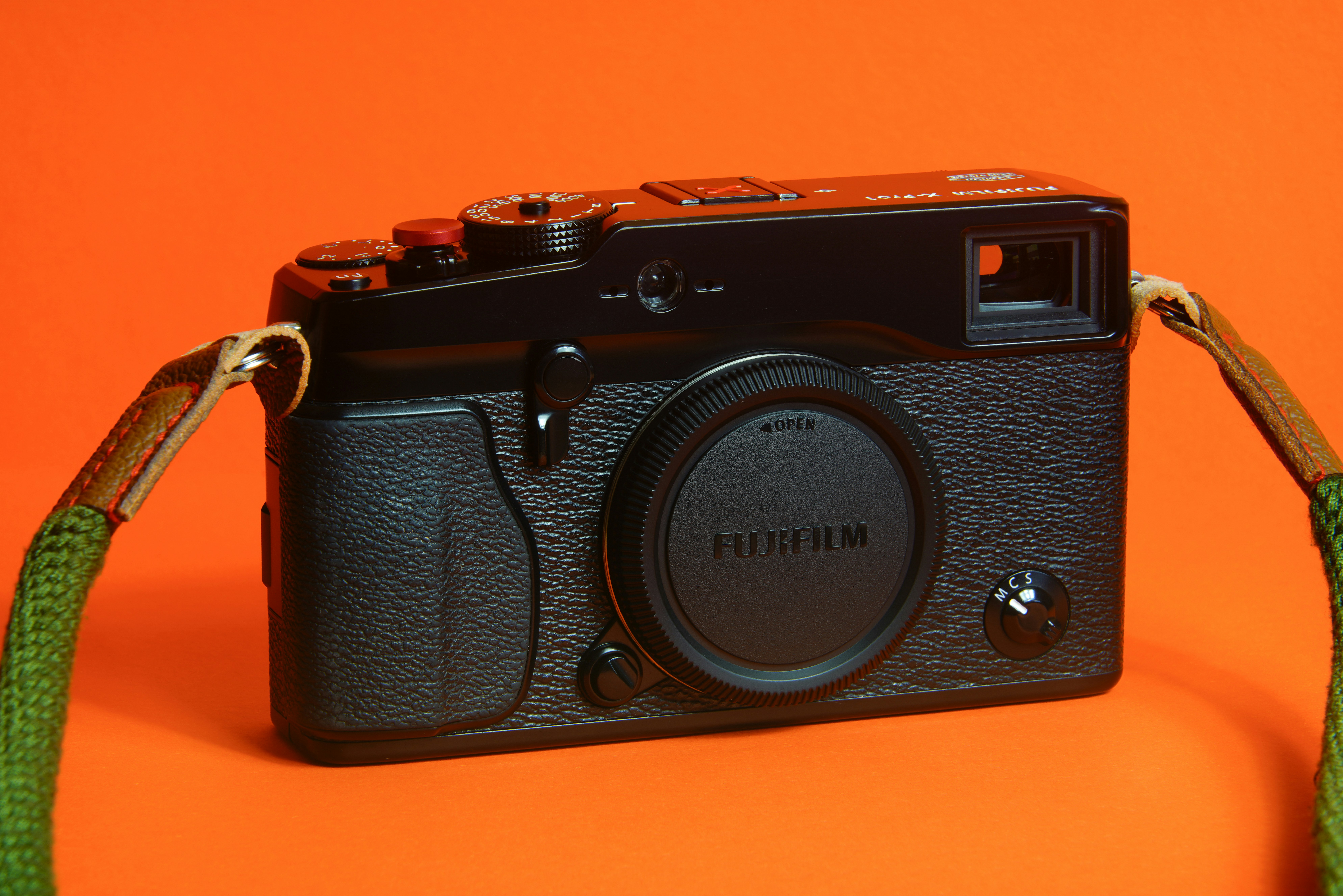 A black camera with a green strap on an orange background