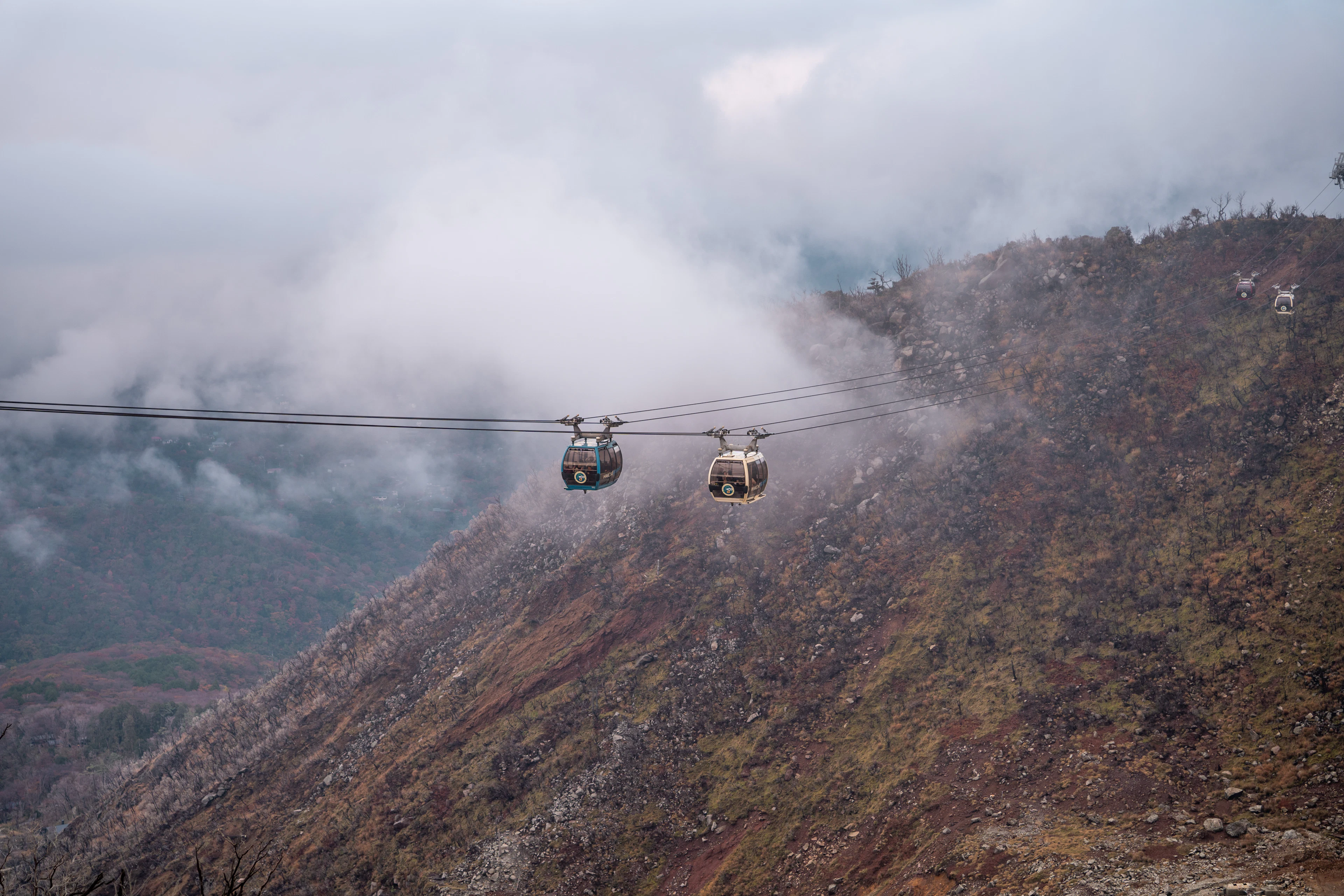 Cable-car gondolas above a volcanic mountainside in drifting cloud