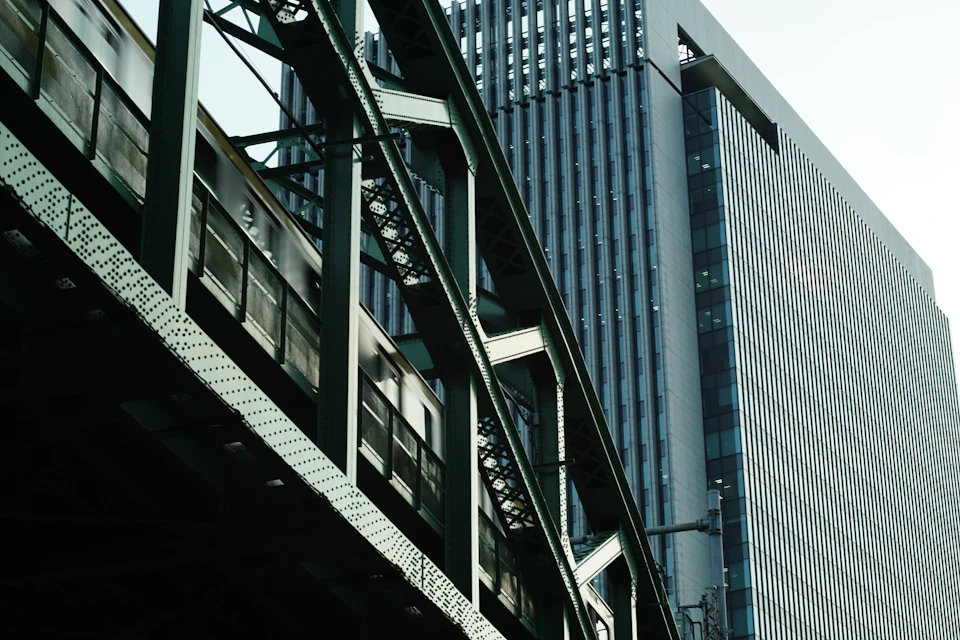 Train crosses over elevated railway track with metal beams and tall glass buildings