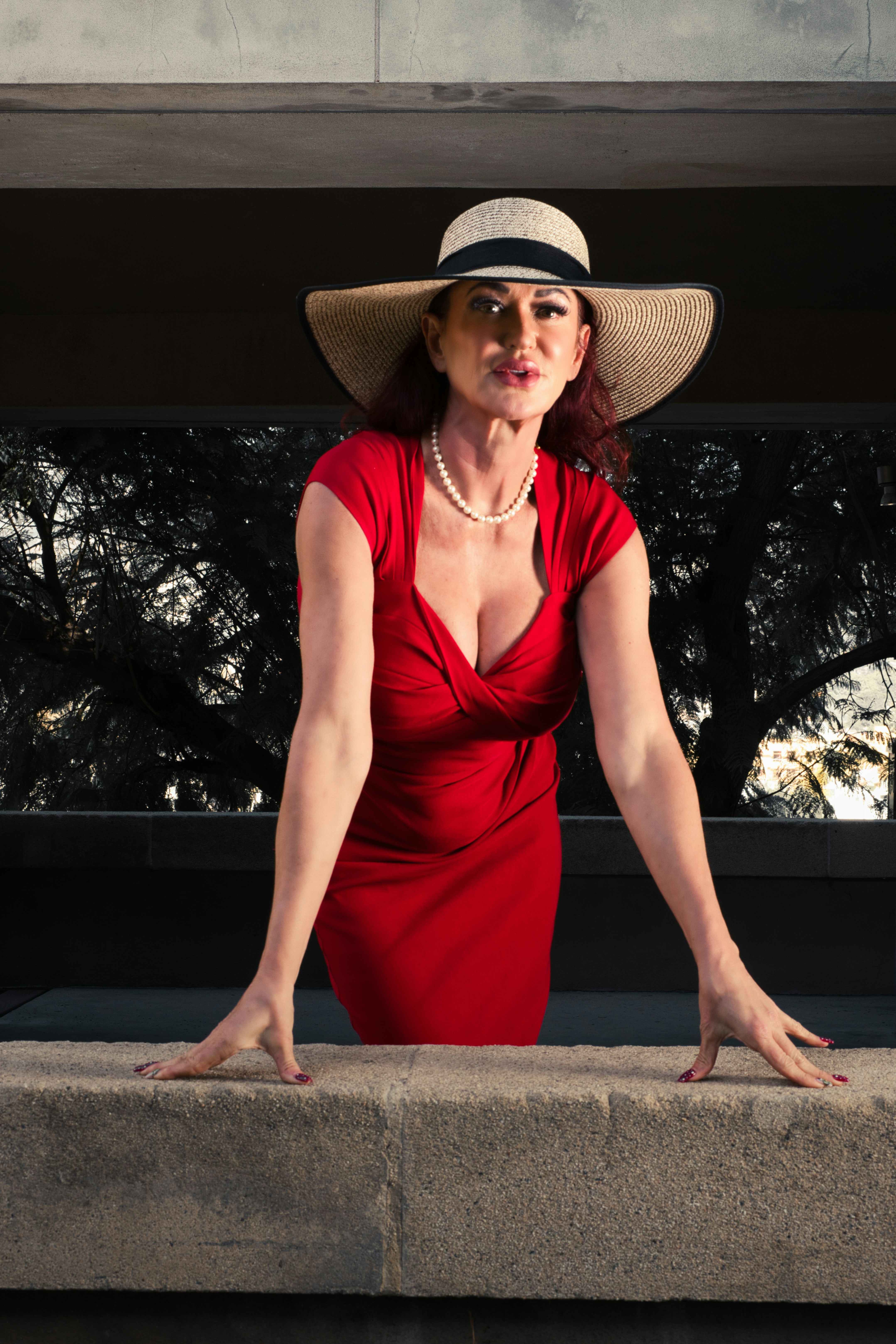 Una mujer con vestido rojo y sombrero apoyada en una repisa