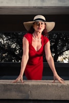 A woman in a red dress and hat leaning on a ledge