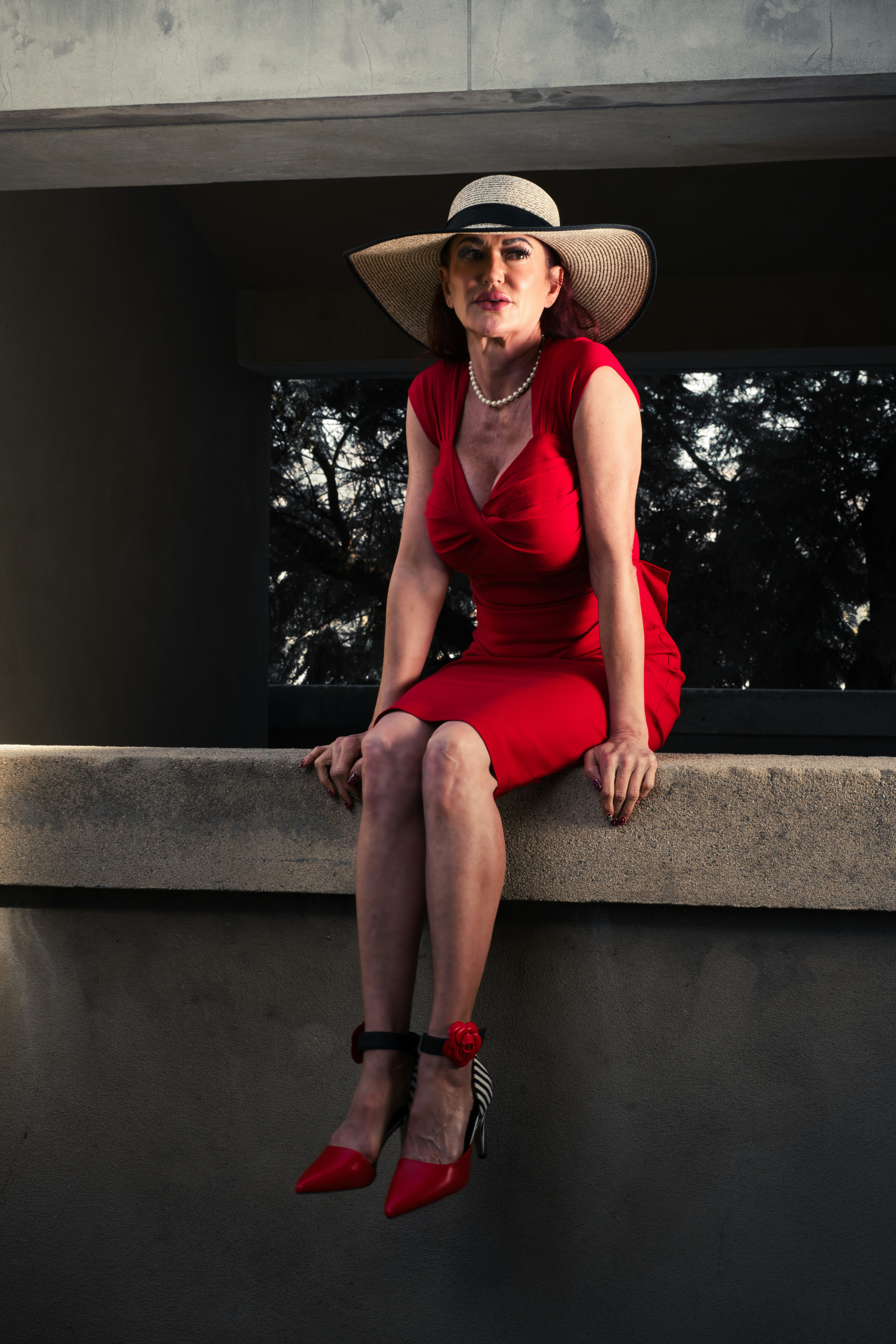 A woman in a red dress and hat sitting on a ledge
