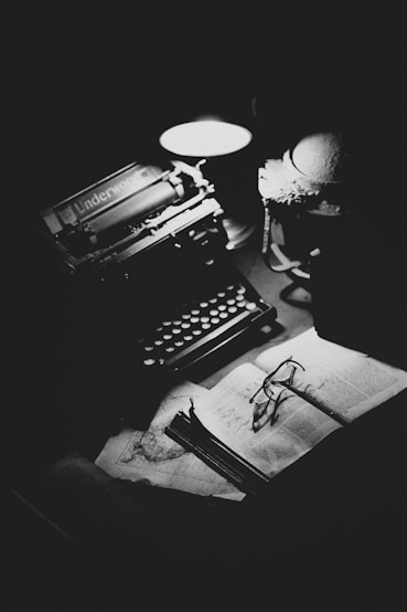 A black and white photo of a desk with a typewriter, lamp, and