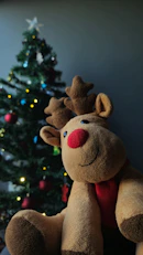 A stuffed reindeer sitting in front of a christmas tree