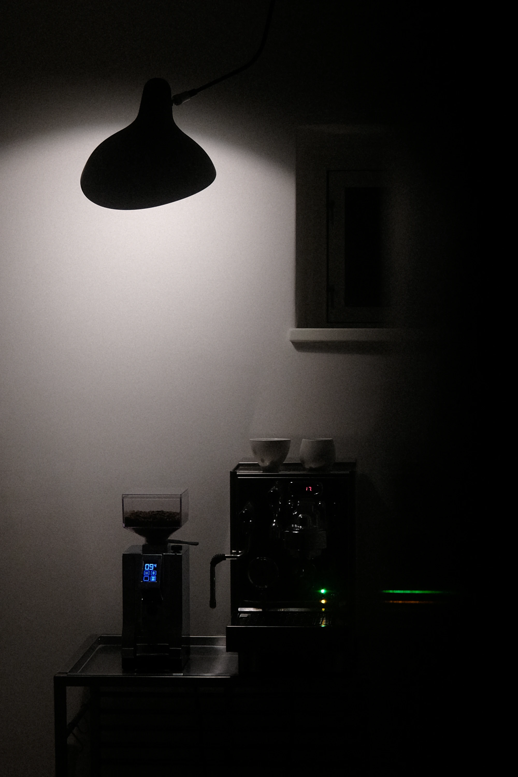 A modern espresso machine and coffee grinder in a softly lit, dark coffee corner