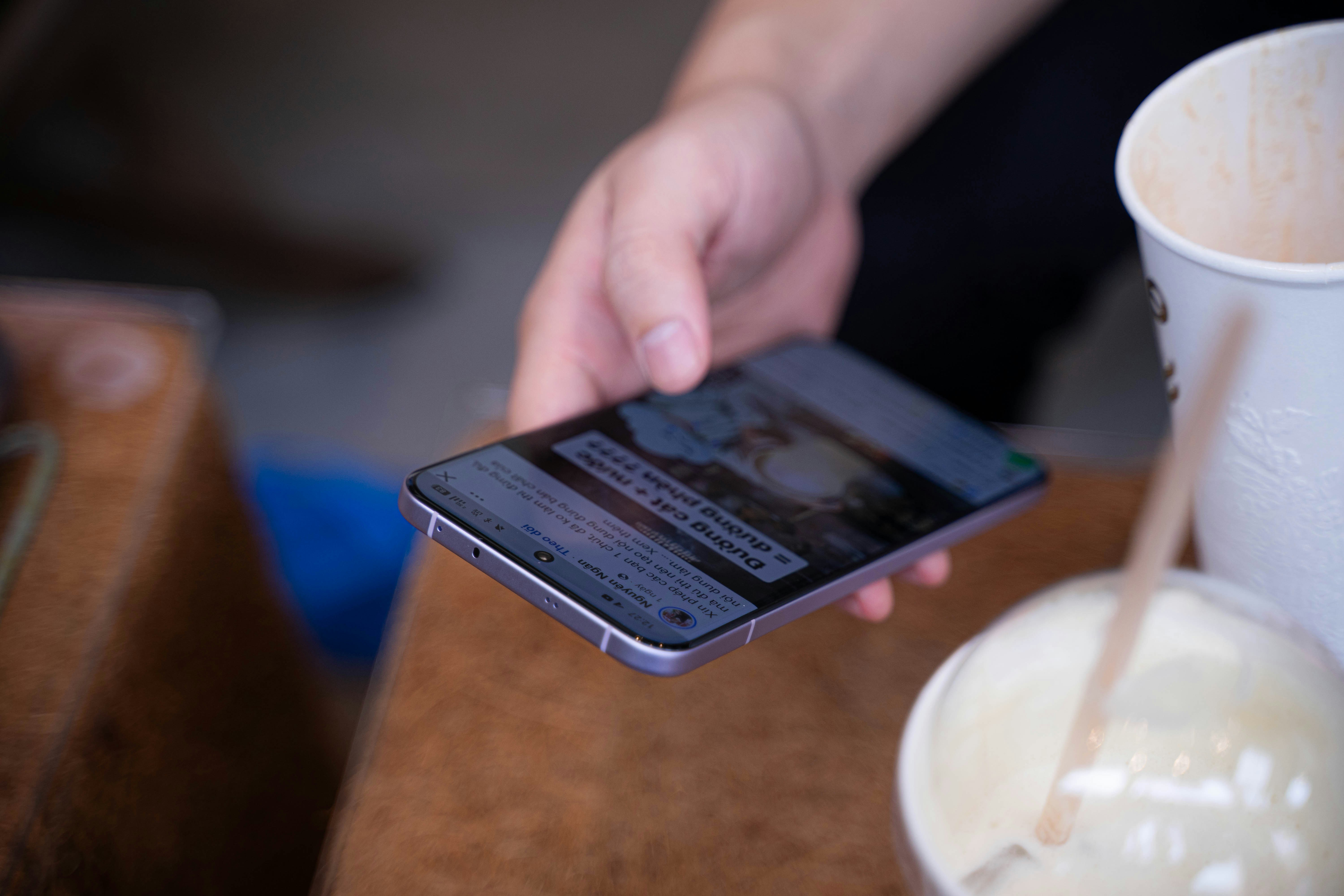 A person holding a cell phone next to a cup of milk