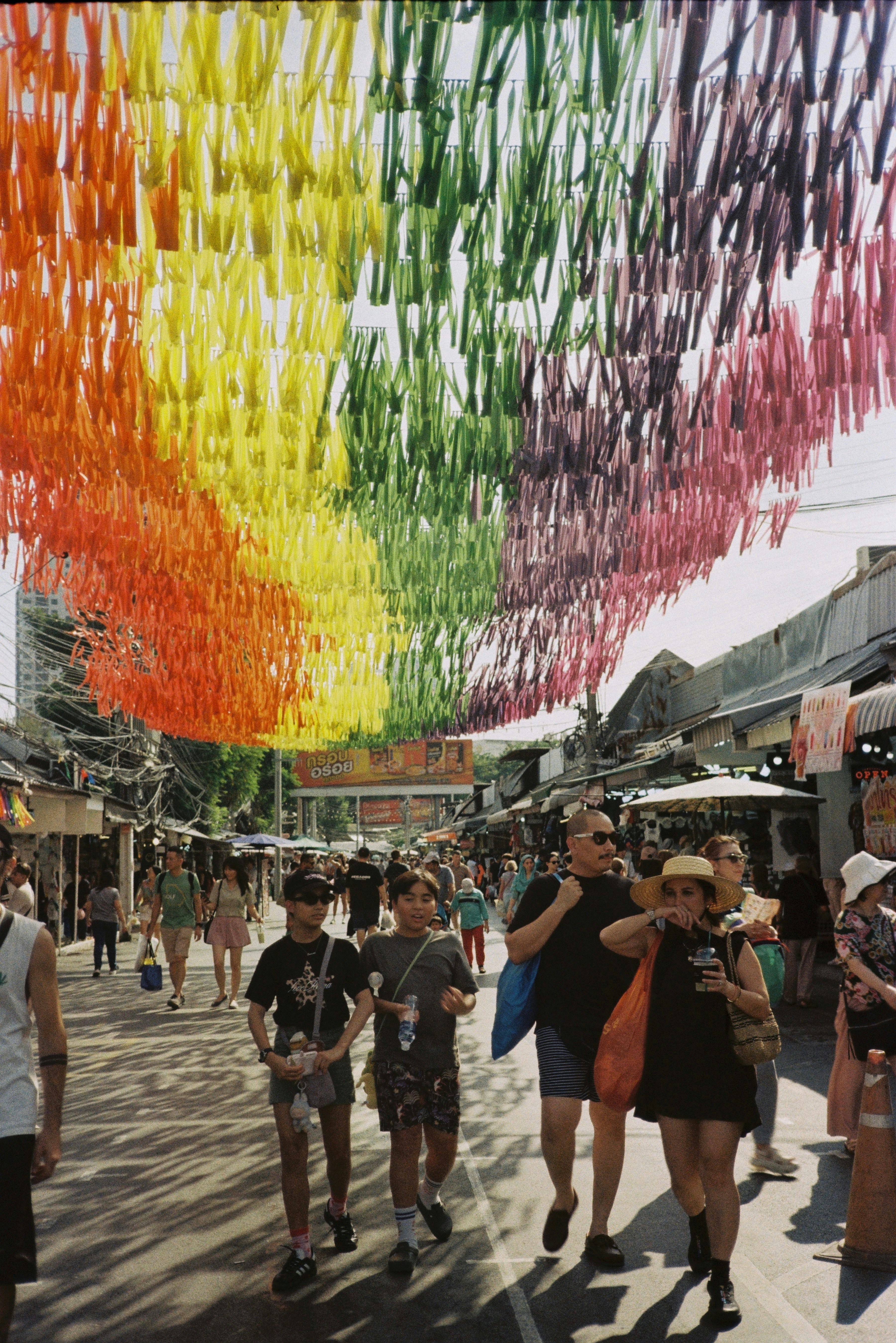 A group of people walking down a street under a rainbow colored stream of streamers