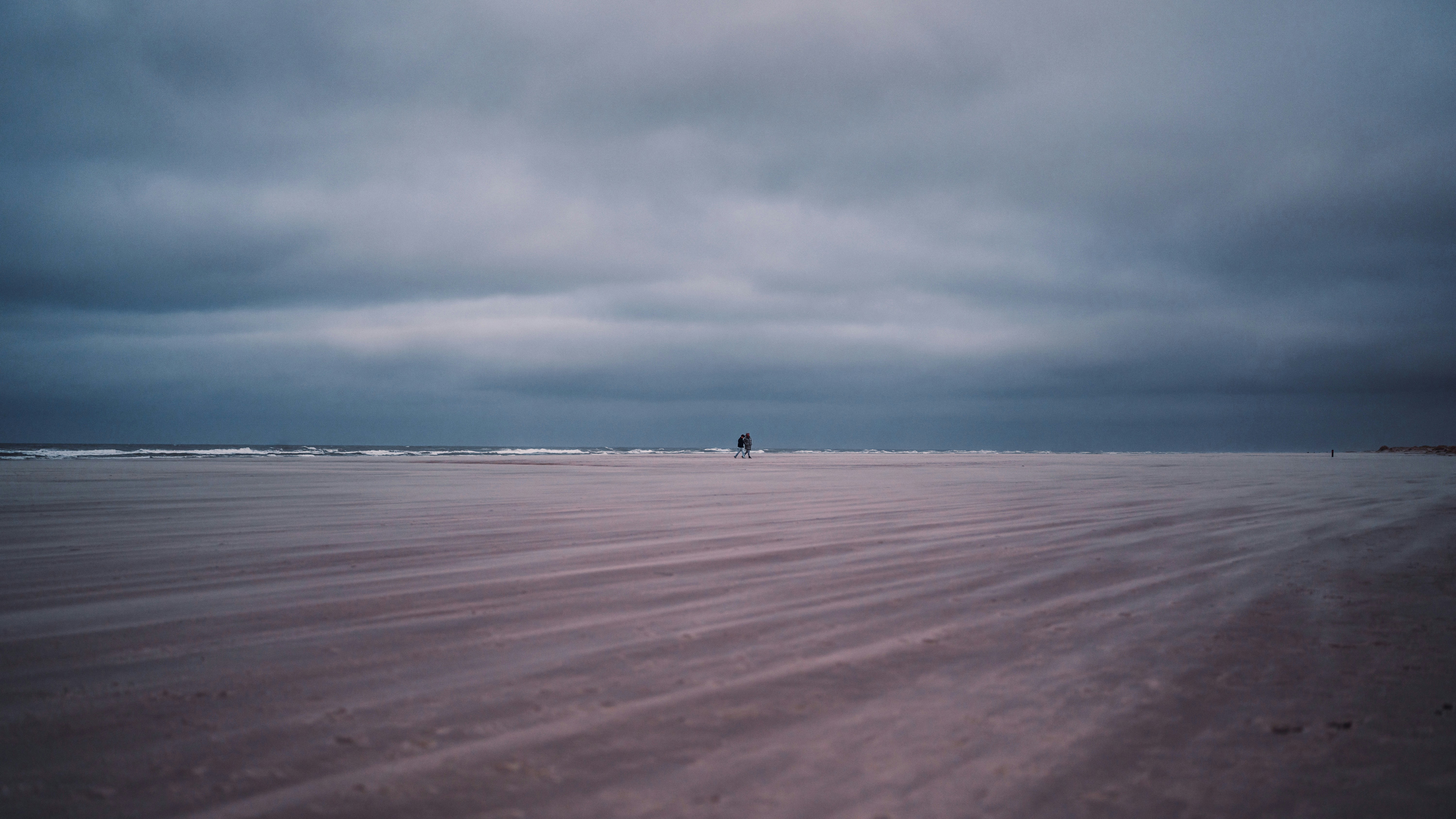 A person walking on a beach under a cloudy sky