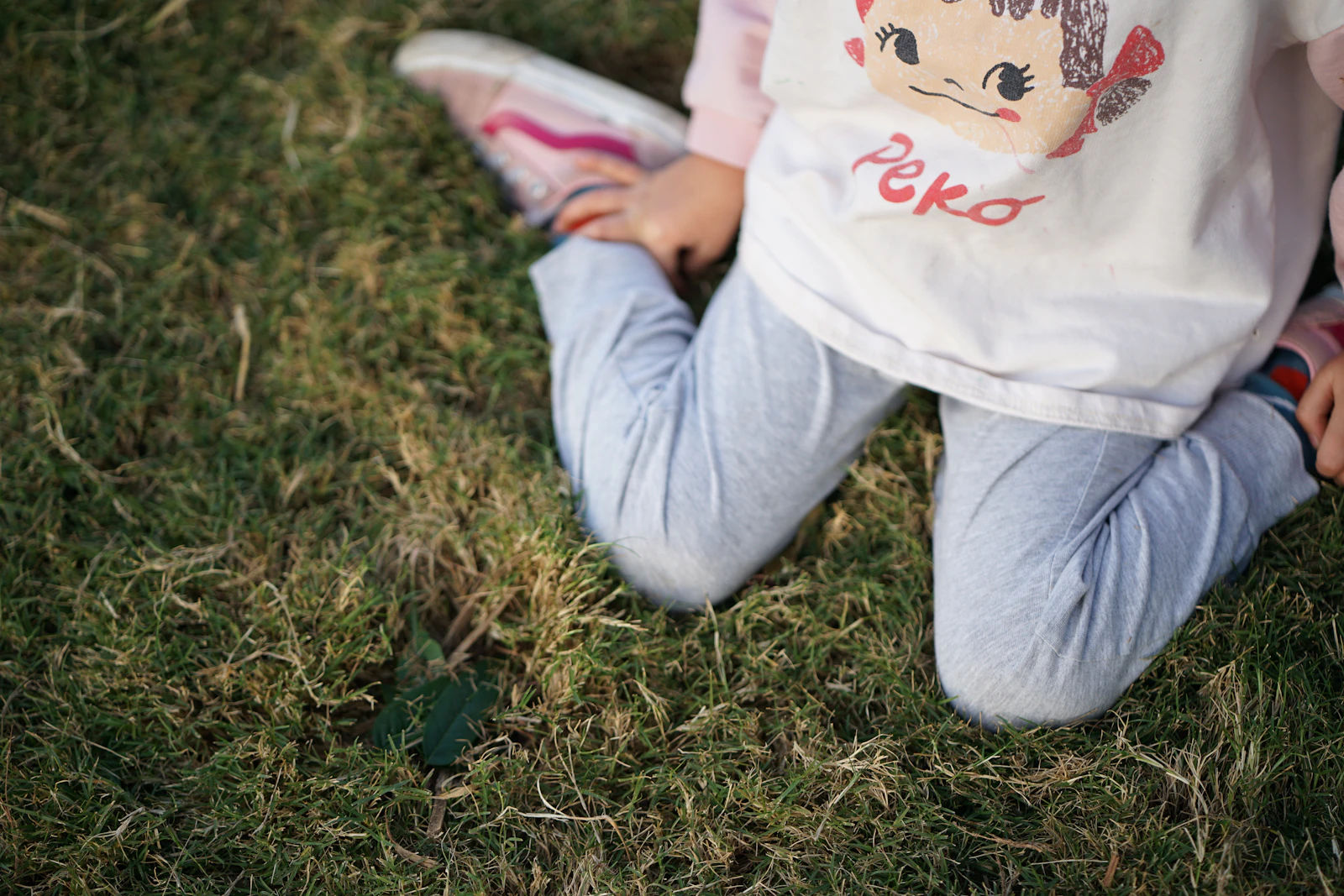 A child's legs in grey cotton trousers lying in long grass