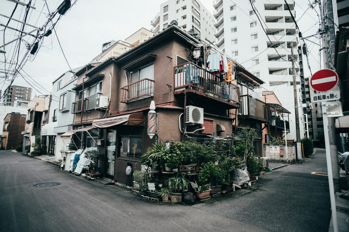 東京の住宅街の交差点に建つ古い木造の建物と、奥に見える集合住宅
