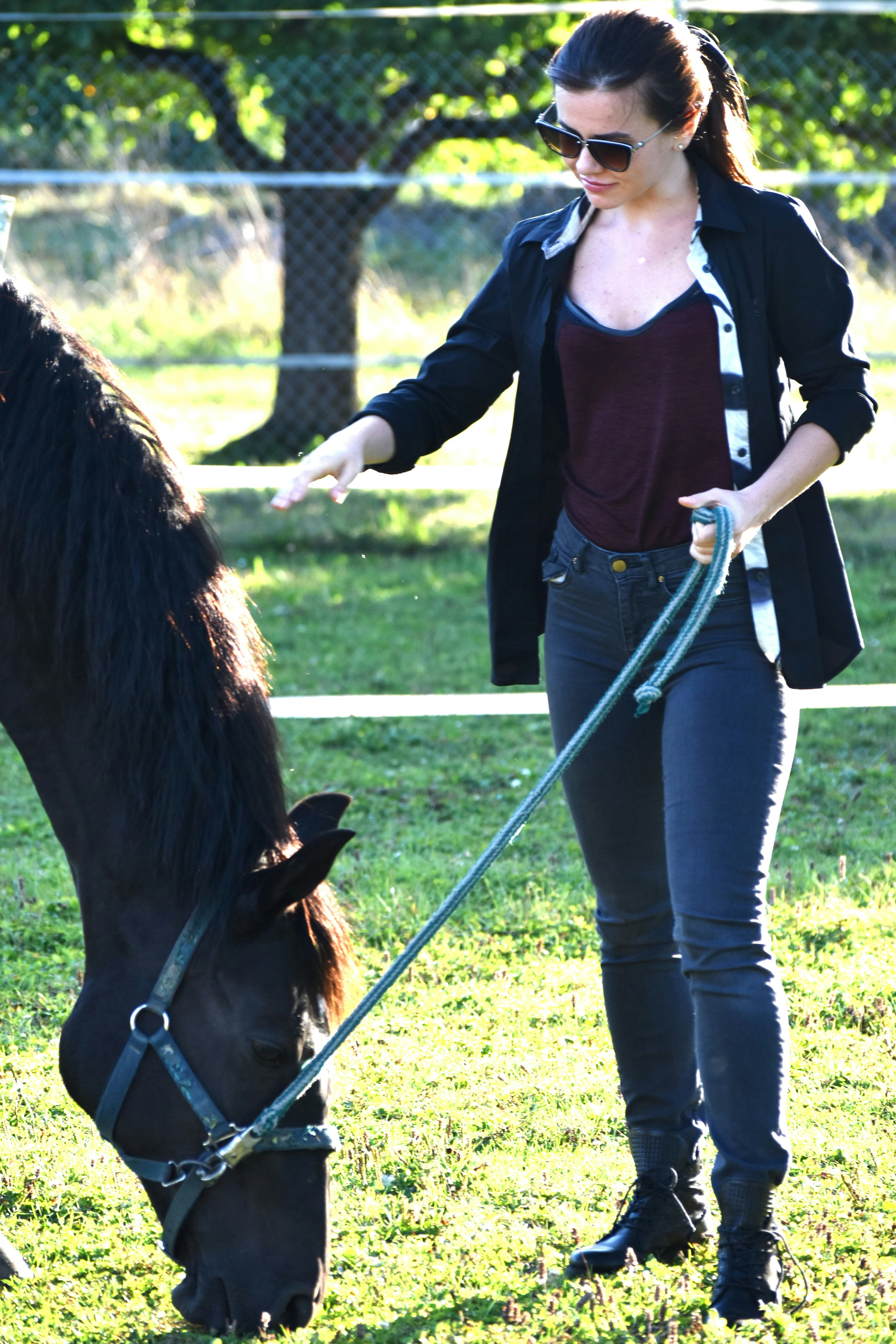 A woman standing next to a horse eating grass