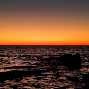 The sun is setting over the ocean with a rock outcropping
