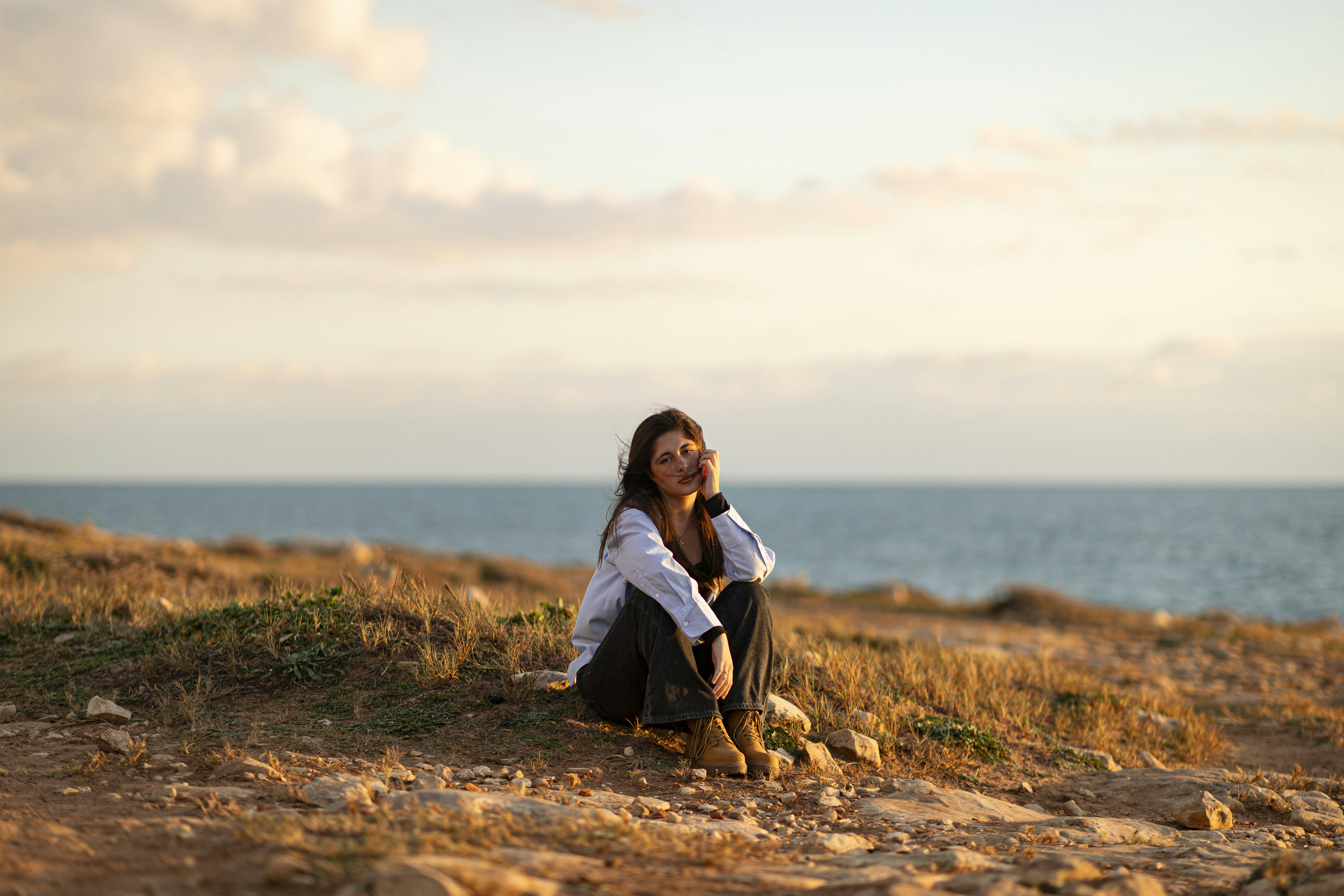 A woman sitting on the ground near the ocean