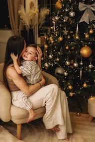 A woman holding a baby in front of a christmas tree