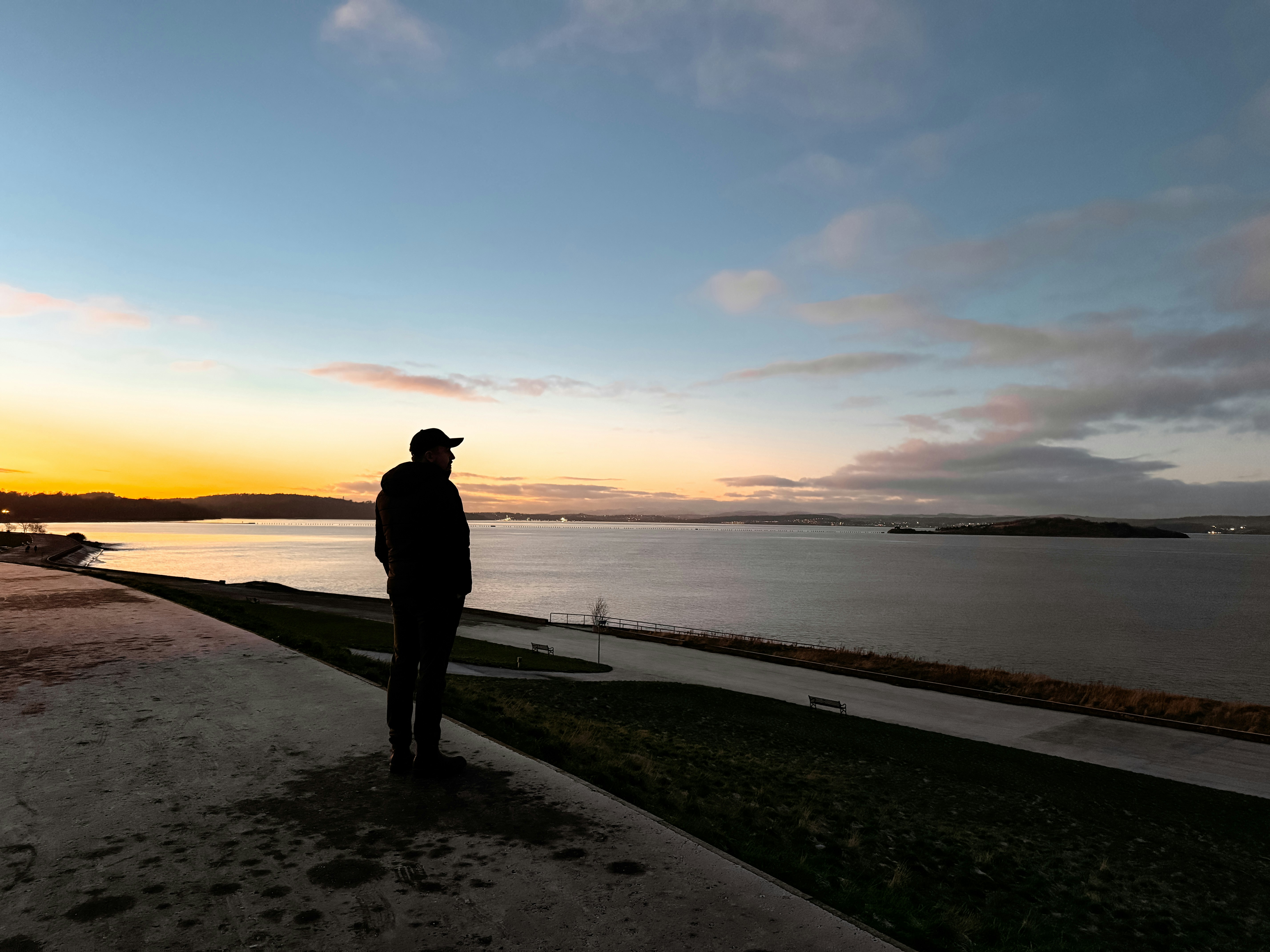 A man standing on a sidewalk next to a body of water