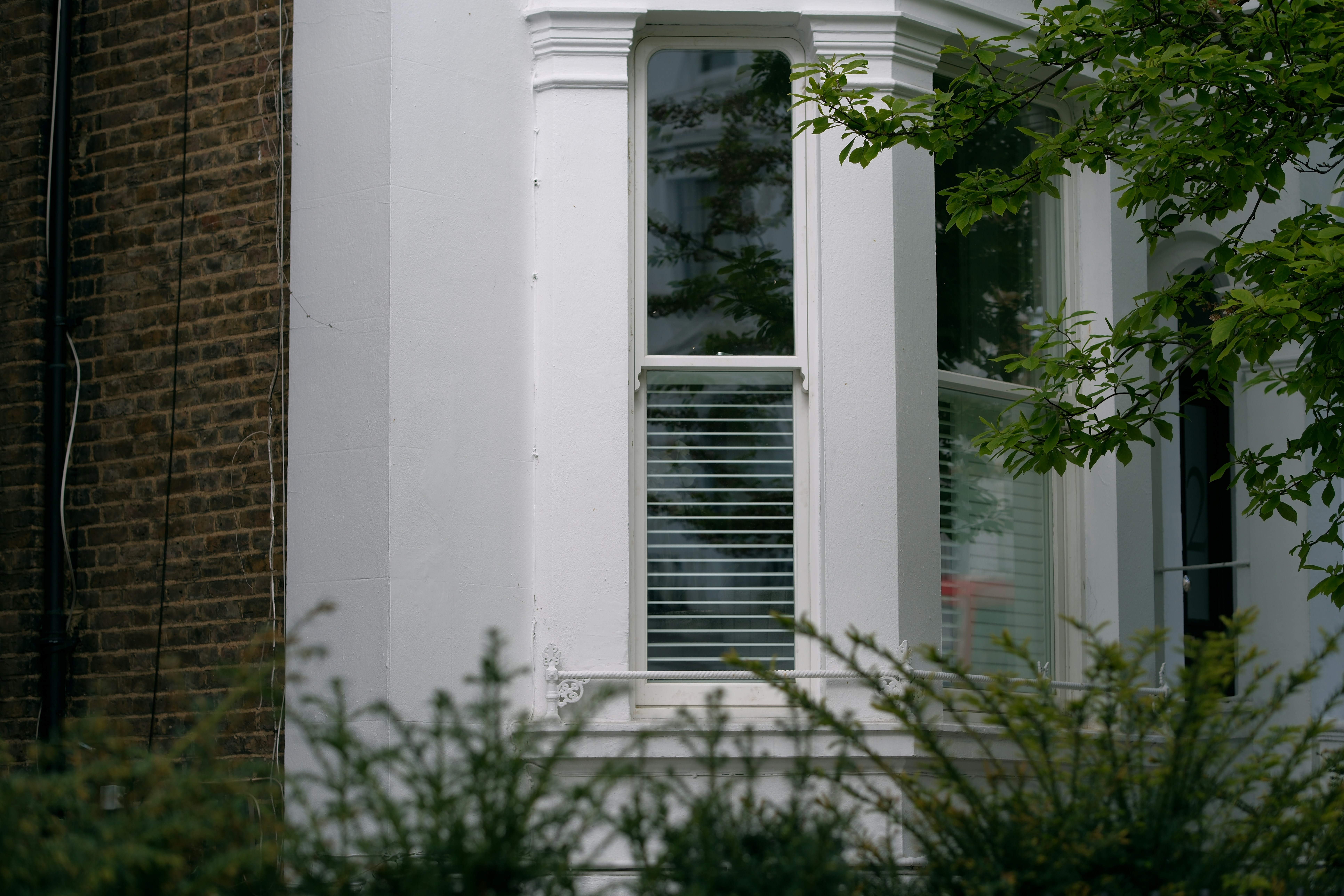 A white window sitting next to a tall brick building photo – Free ...