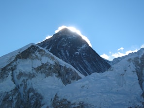 A snow covered mountain with the sun peeking through the clouds