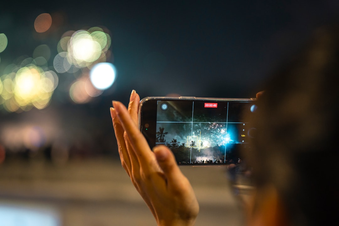 A person reading a glowing live news feed on a smartphone at night