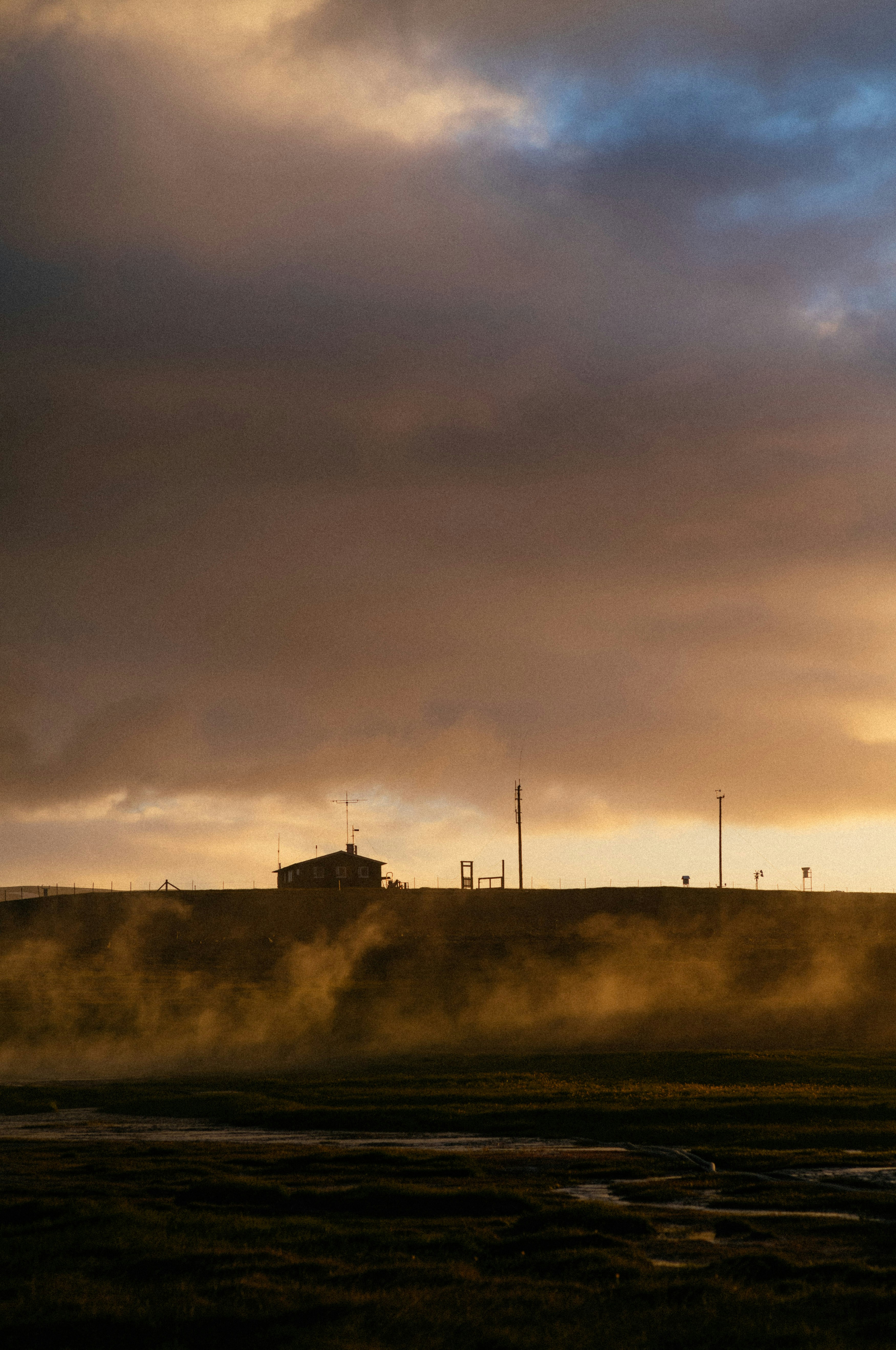 A train traveling past a factory under a cloudy sky
