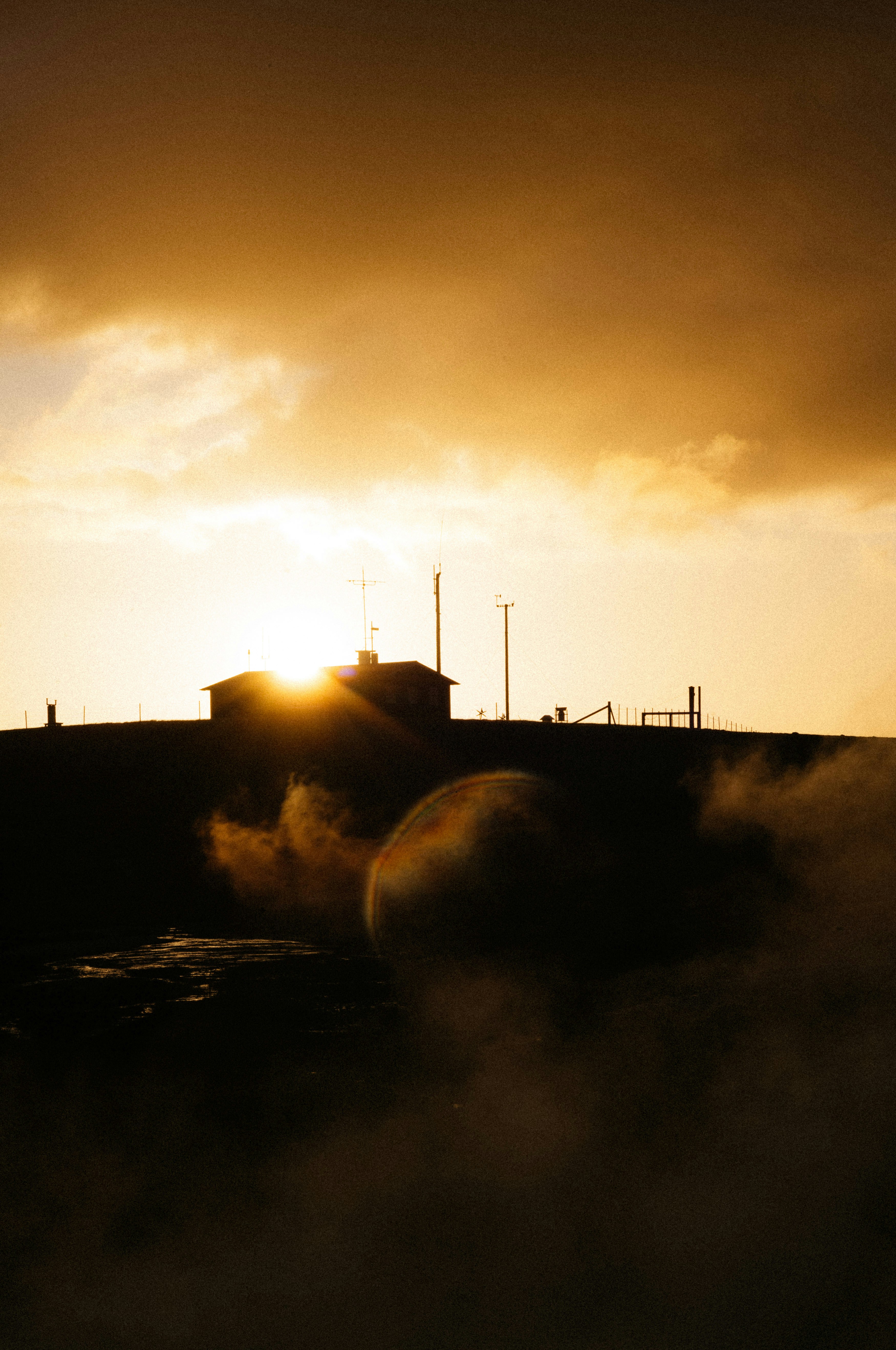 The sun is setting behind a building with smoke coming out of it