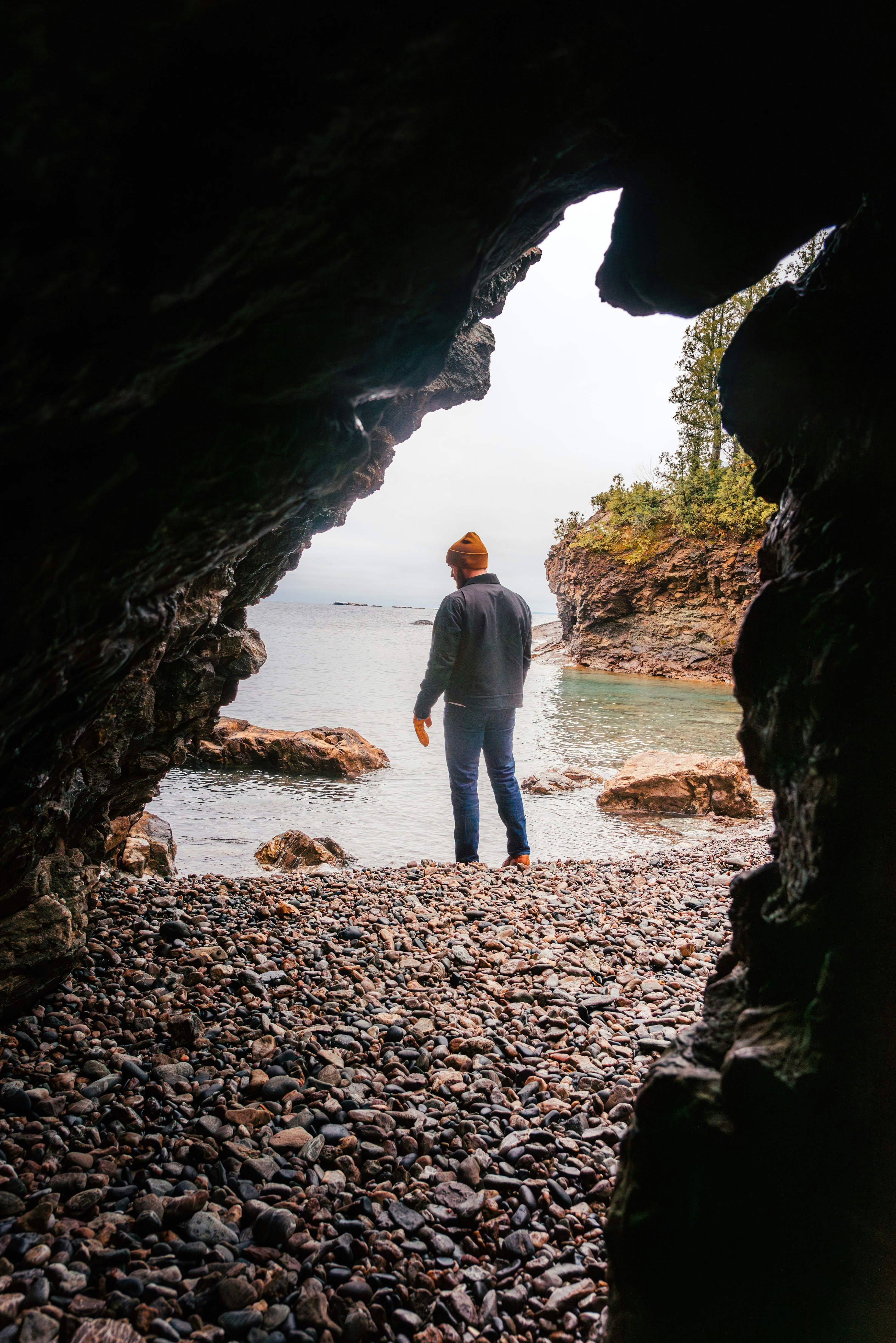 A man standing in a cave looking out at the water