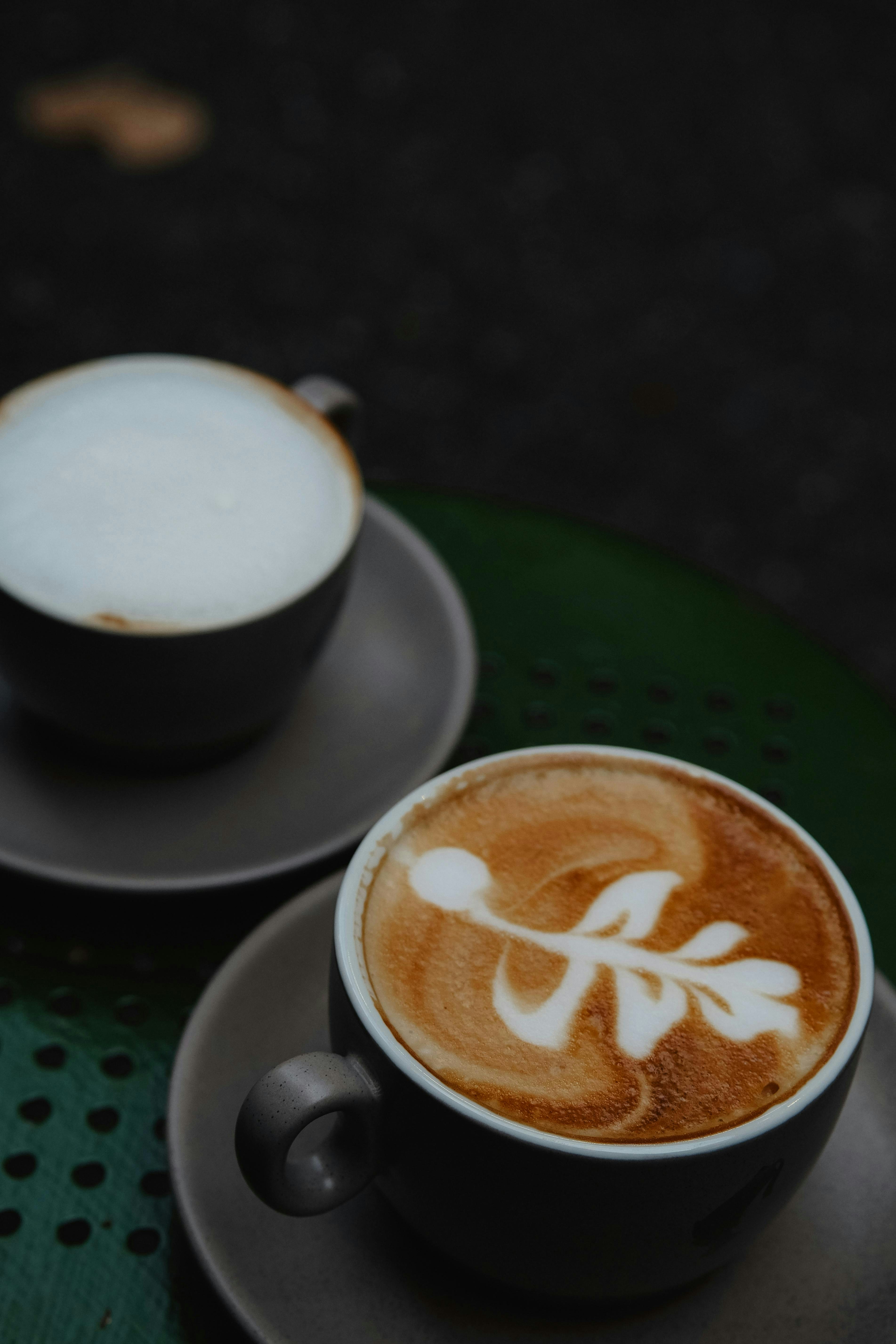 Two cups of coffee sitting on top of a green table