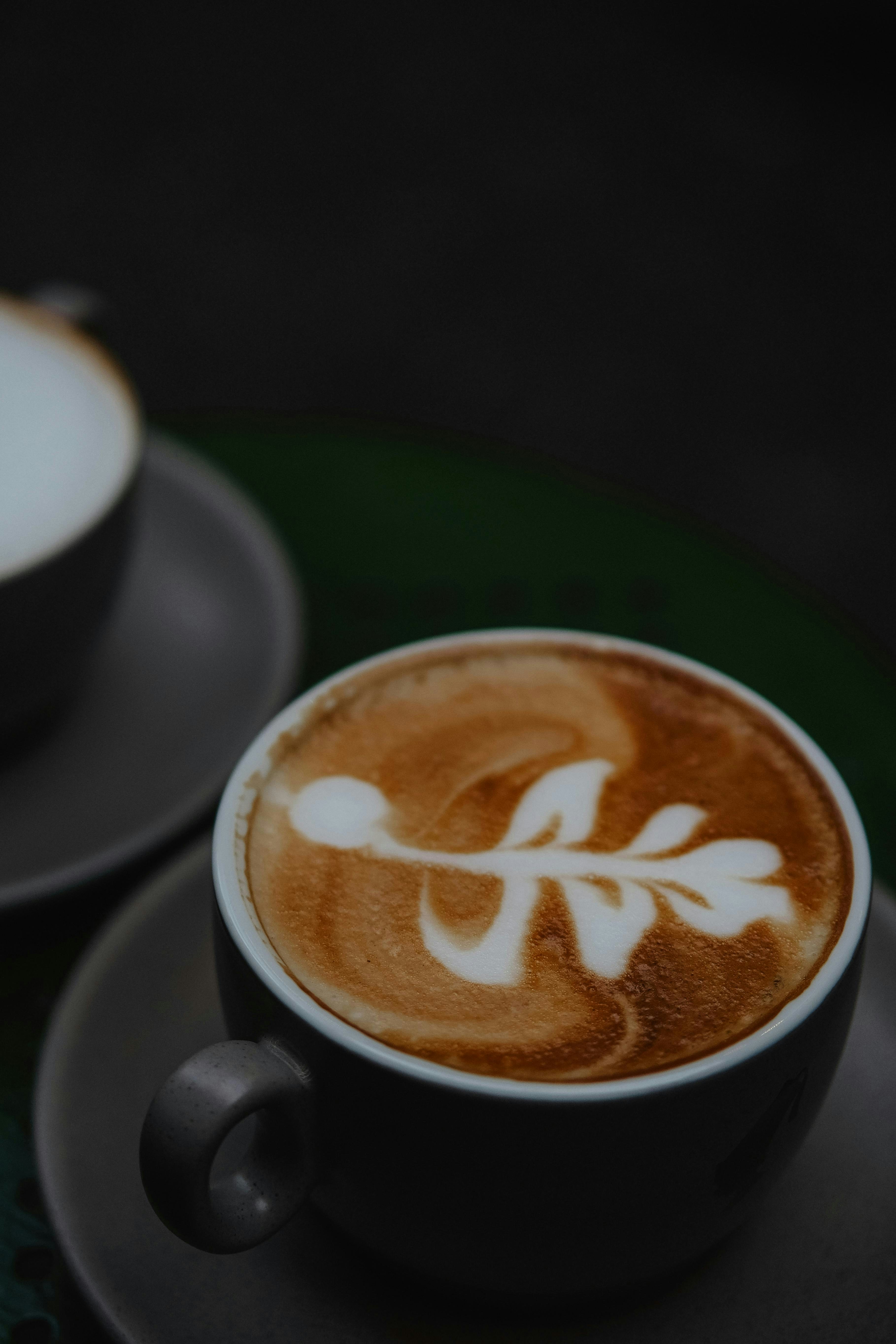 A cappuccino on a saucer next to a cup of coffee