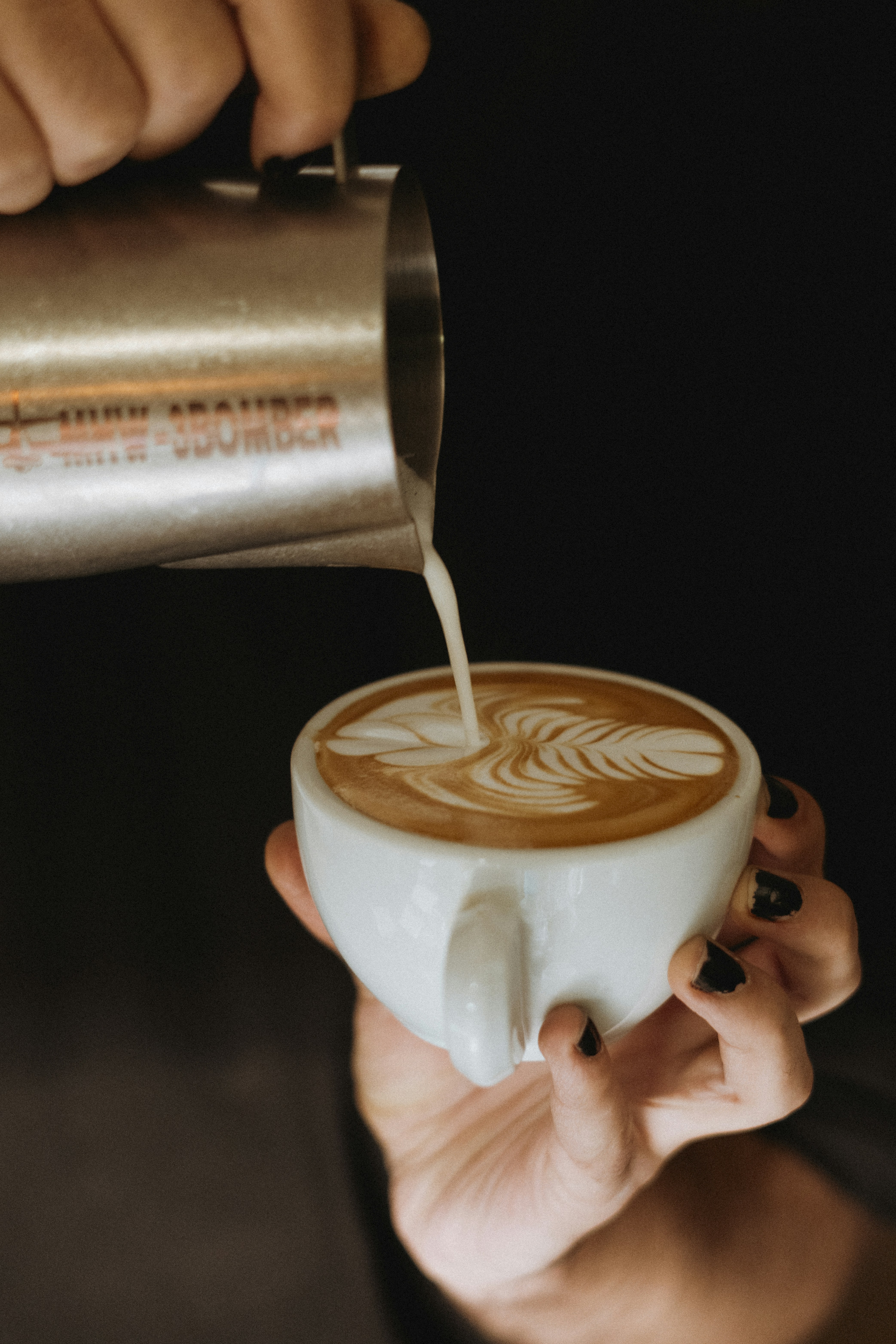 A person pouring milk into a cup of coffee