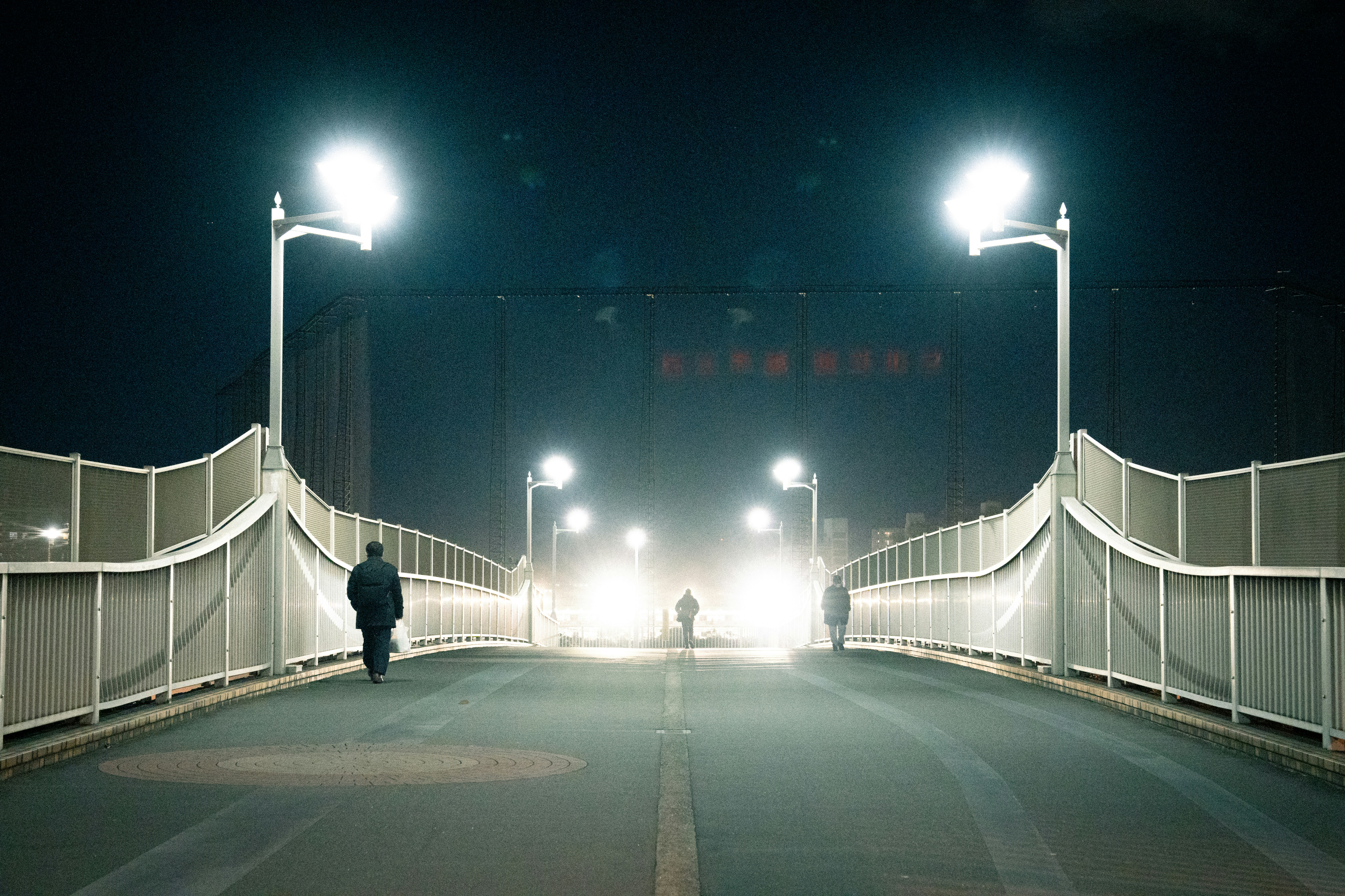 A man walking across a bridge at night