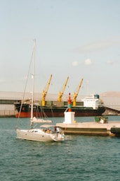 A boat is docked at a dock with a cargo ship in the background