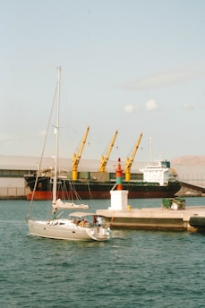 A boat is docked at a dock with a cargo ship in the background